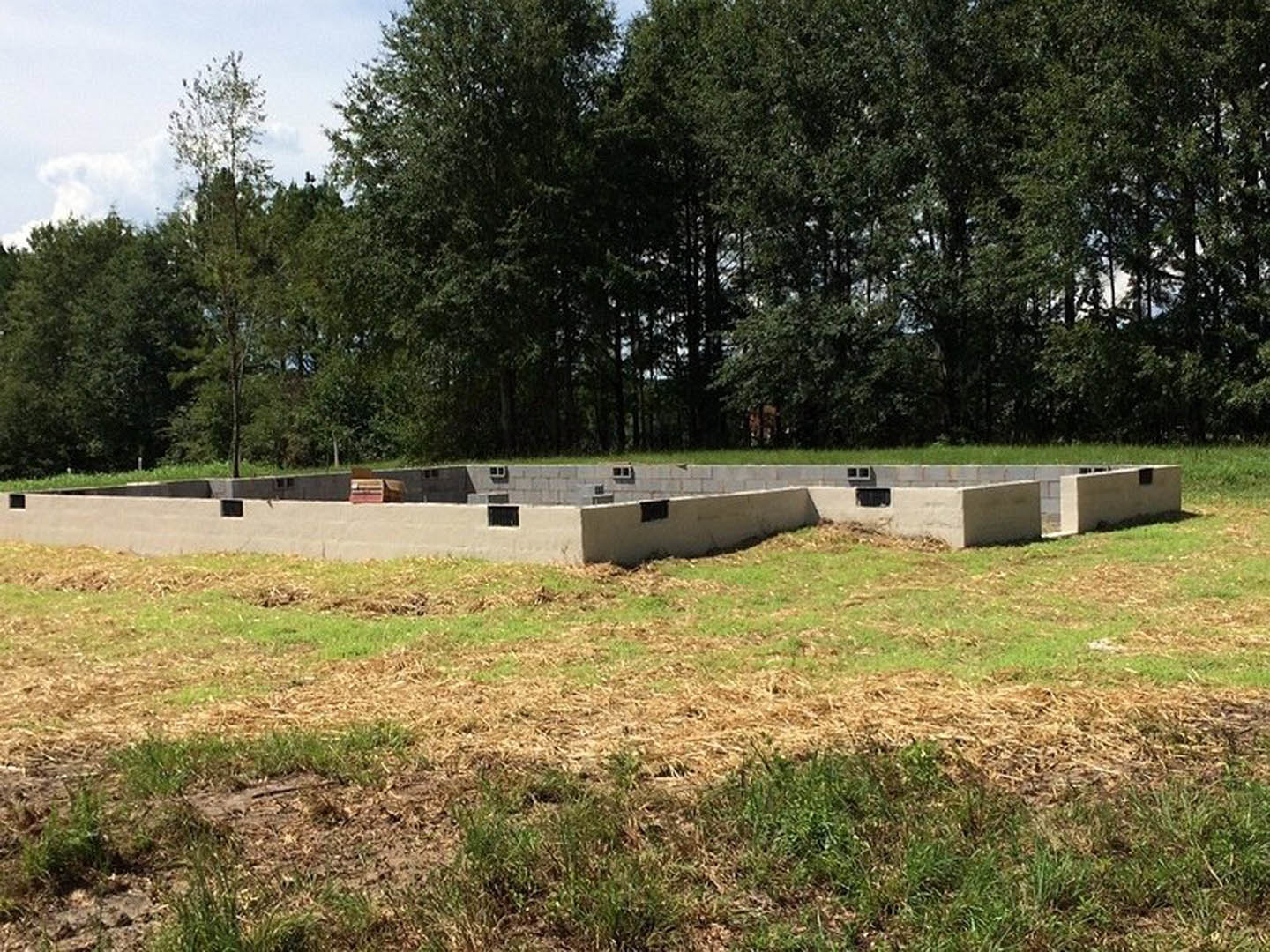 Concrete foundation slab set in a grassy field with trees in the background and a square window opening in the wall