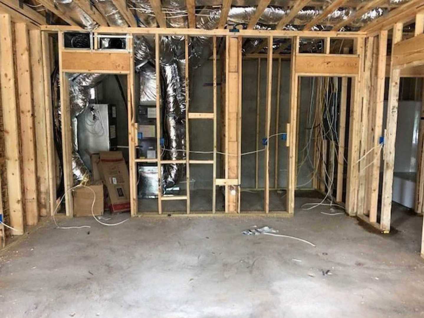Unfinished room with exposed wooden framing, concrete floor, metal pipe, electrical wires, and blurry window in background