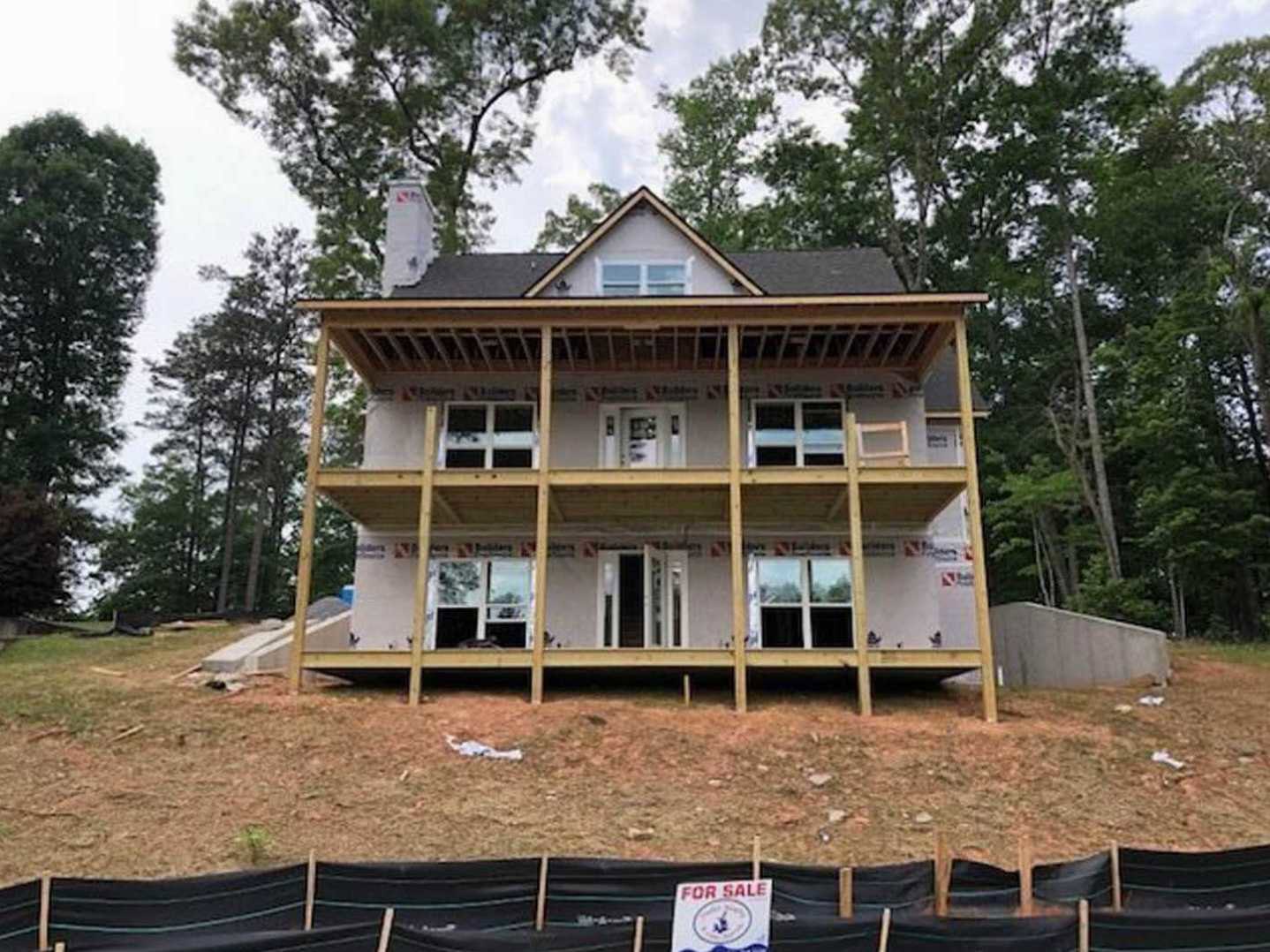 Framed house under construction with exposed wood, white door with glass panels, white-framed window, surrounding trees, and construction signs in foreground