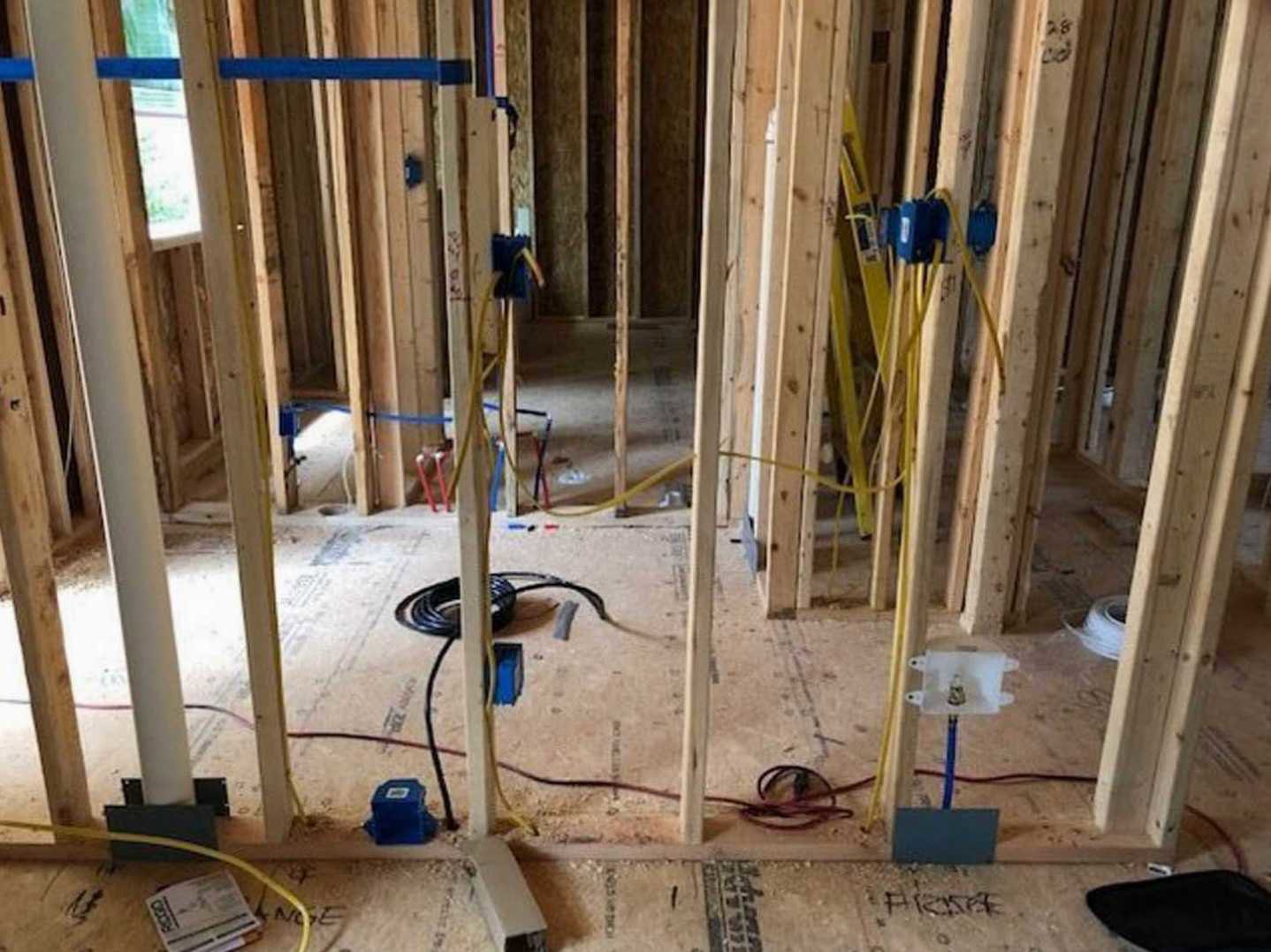 Unfinished room with exposed wood framing, visible electrical wires, and construction materials scattered on surfaces
