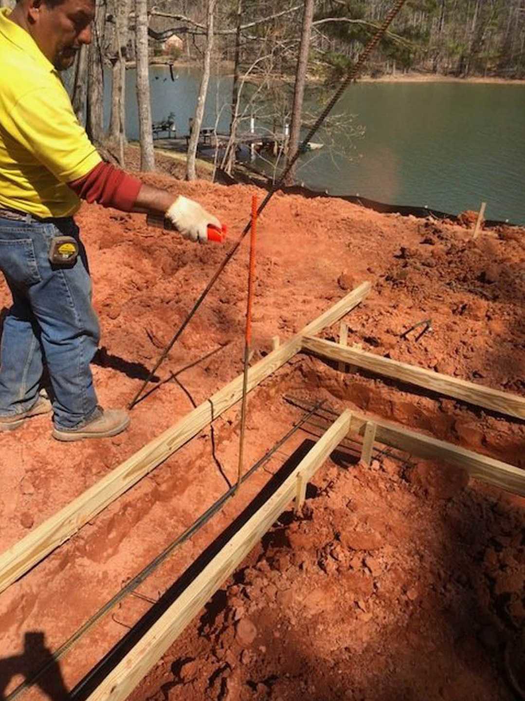 Man in yellow shirt and blue jeans shoveling soil on custom home construction site with exposed ground and building materials