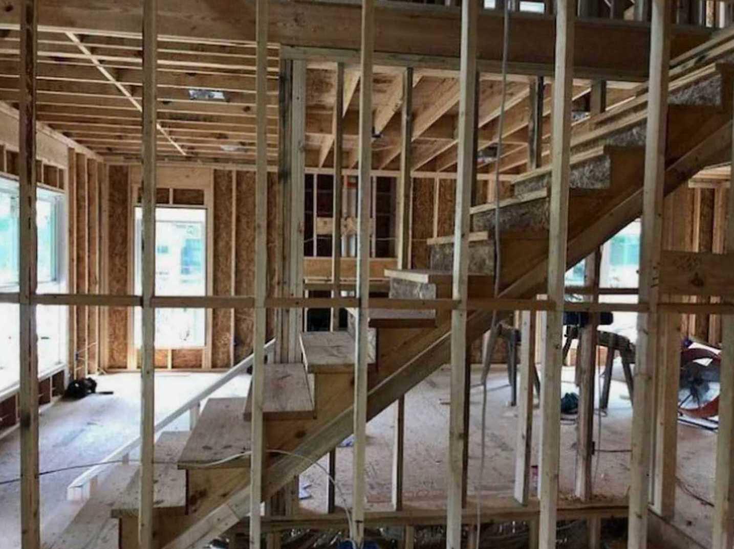 Unfinished wooden staircase with exposed beams and construction materials in a partially built interior space