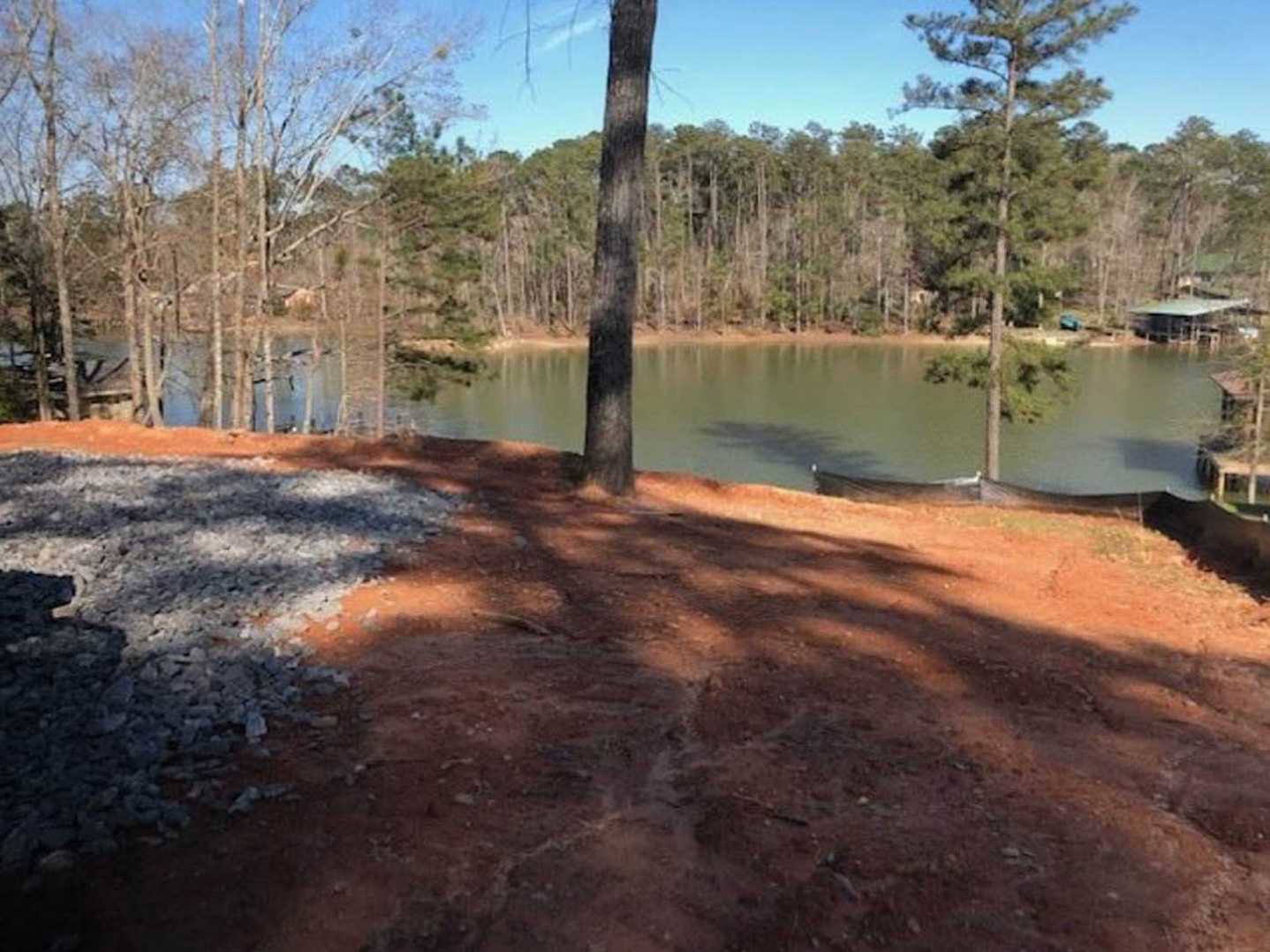 Modern lakeside home with wood siding, large windows, and landscaped yard overlooking calm water and surrounding trees