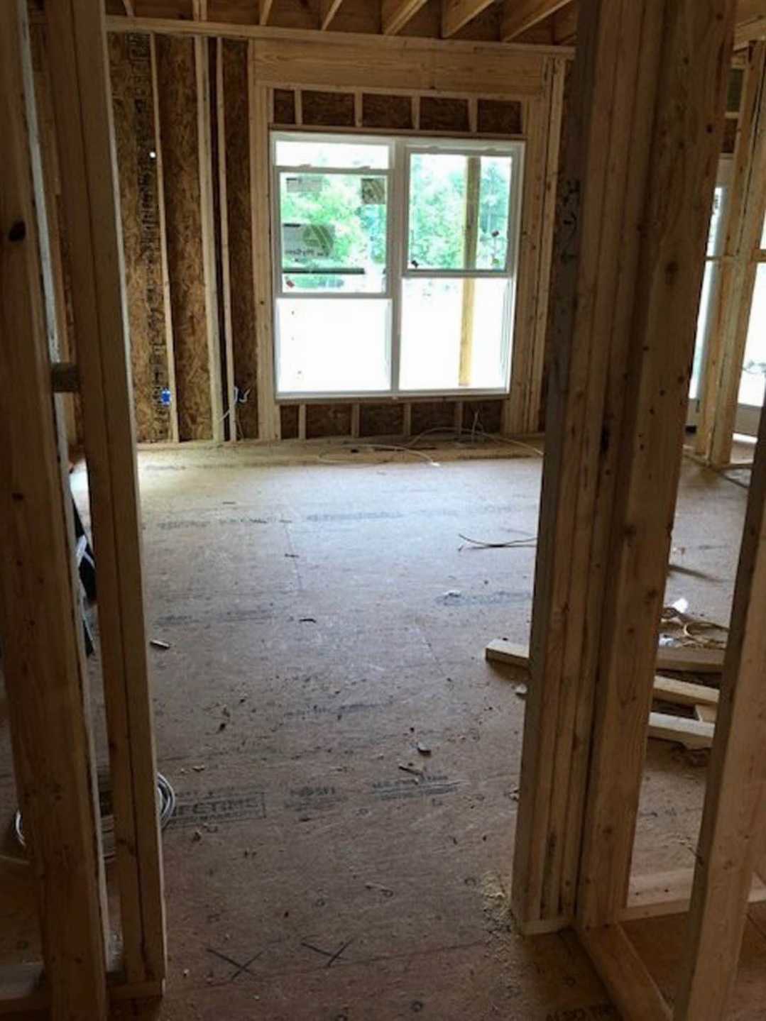 Room under construction with exposed wood framing, multiple windows, wood beams, unfinished plank flooring, and a door.