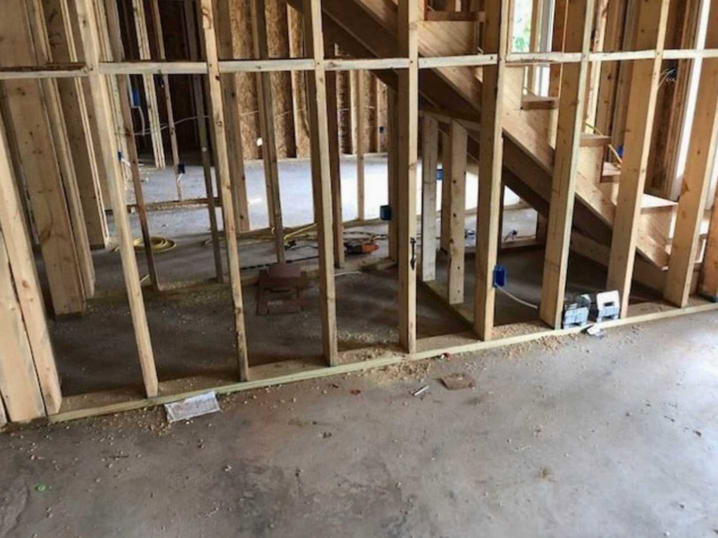 Exposed wood framing with beams and posts inside an unfinished residential room, construction materials visible on the floor