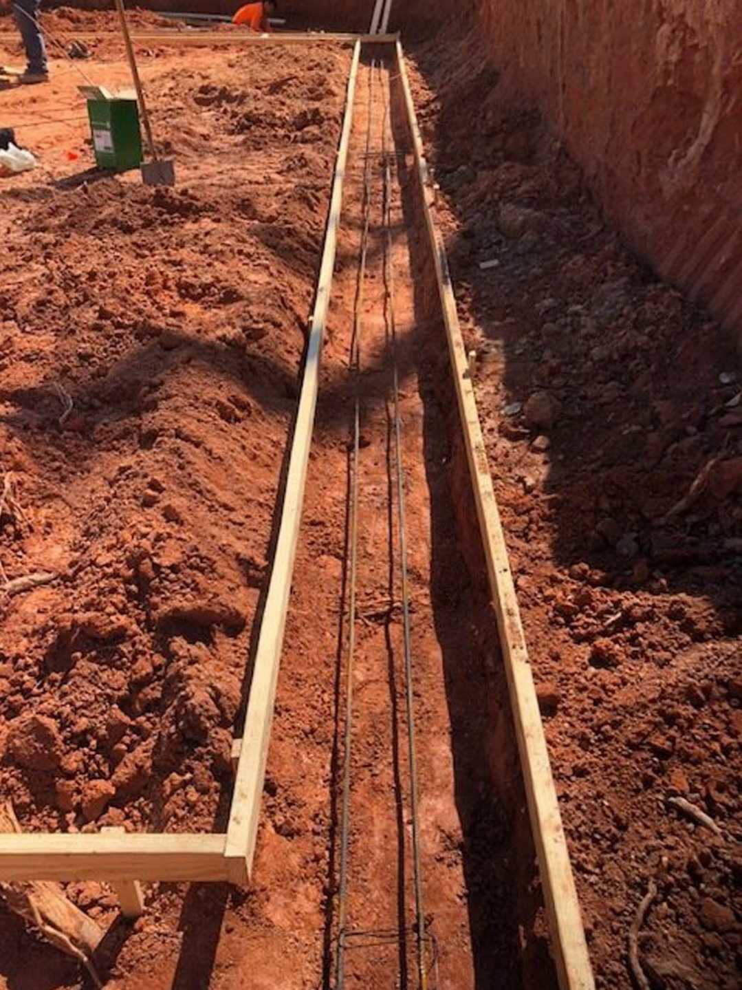 Wooden beam positioned in a dirt pit at an outdoor residential construction site, surrounded by soil and construction materials.