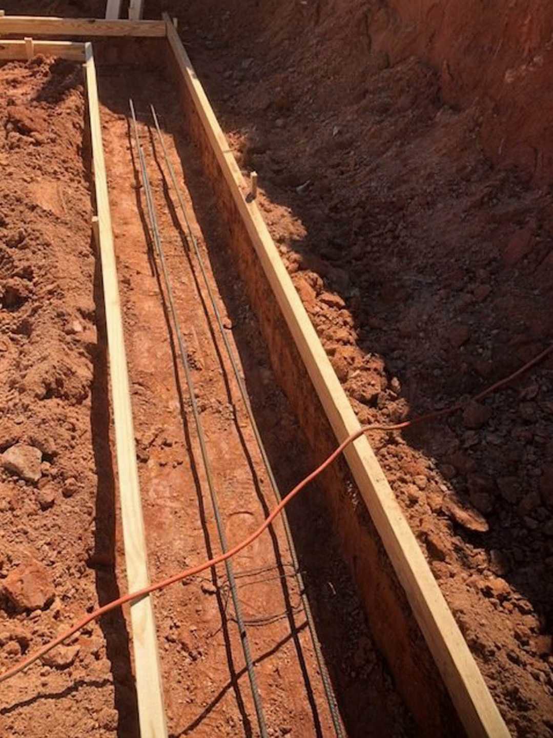Wood beams and metal rods laid in a dirt trench with exposed wires and scattered brown rocks