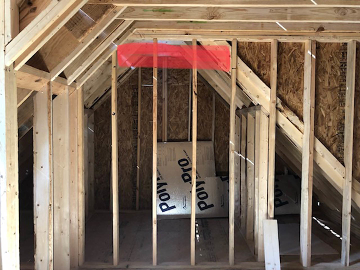 Exposed wooden framing and beams with building insulation, unfinished walls, and a red and black carpet in a residential interior under construction