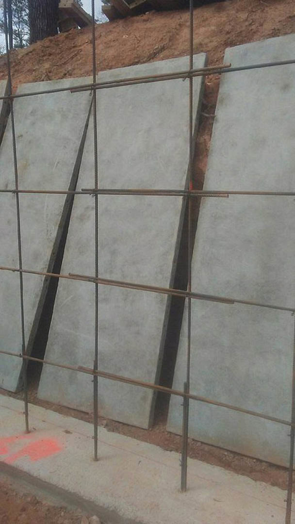 Concrete slab with embedded metal bars, red paint marking on ground, dirt hill in background