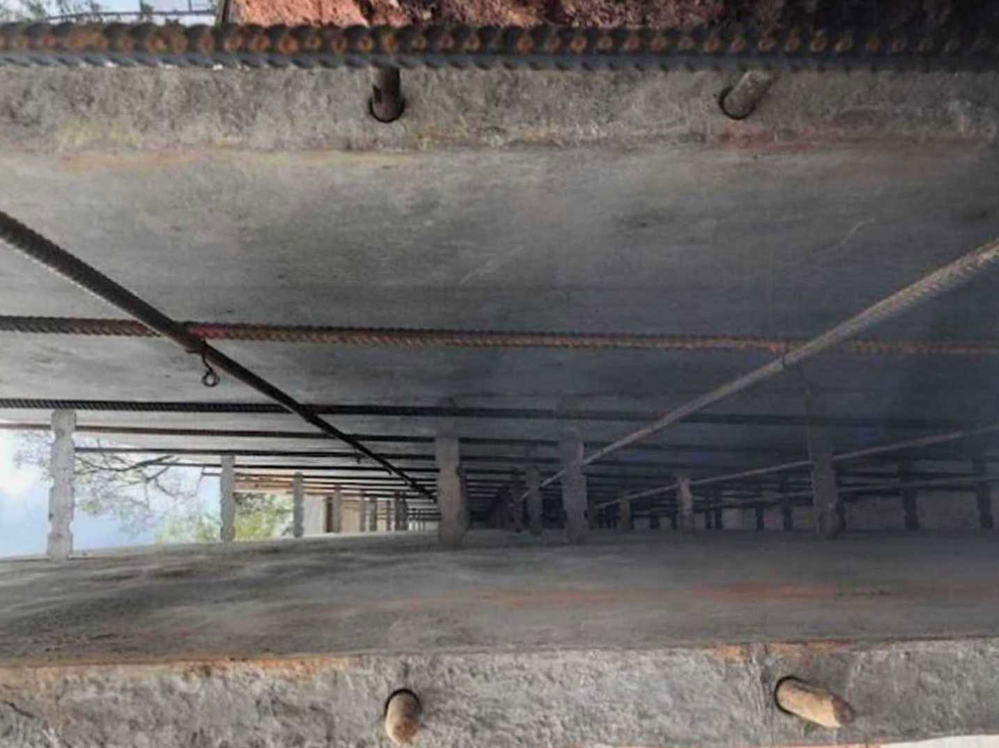 Concrete exterior wall with exposed metal rods, adjacent to outdoor ground and sky.
