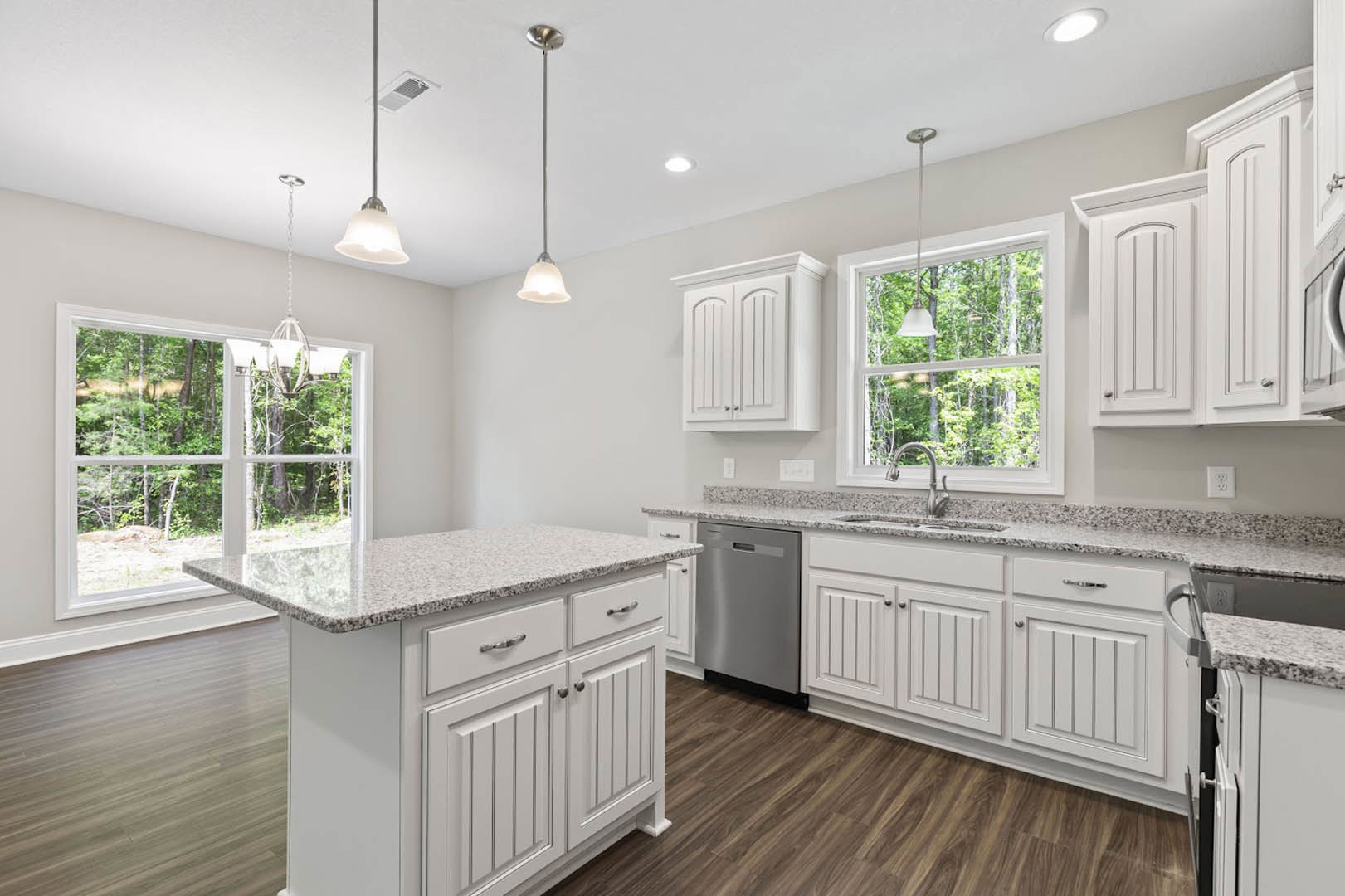 White kitchen with granite countertops, central island, stainless steel refrigerator, ceiling light, and window overlooking trees.
