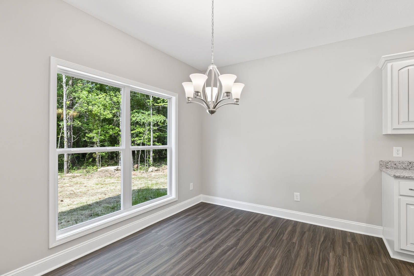 Bright room with large window overlooking trees, wood flooring, white-shaded chandelier, and neutral walls