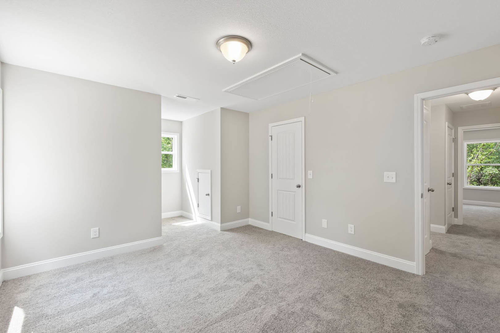 Carpeted room with white walls, white door featuring a silver knob, ceiling-mounted light fixture, window overlooking trees, and decorative molding along the ceiling.