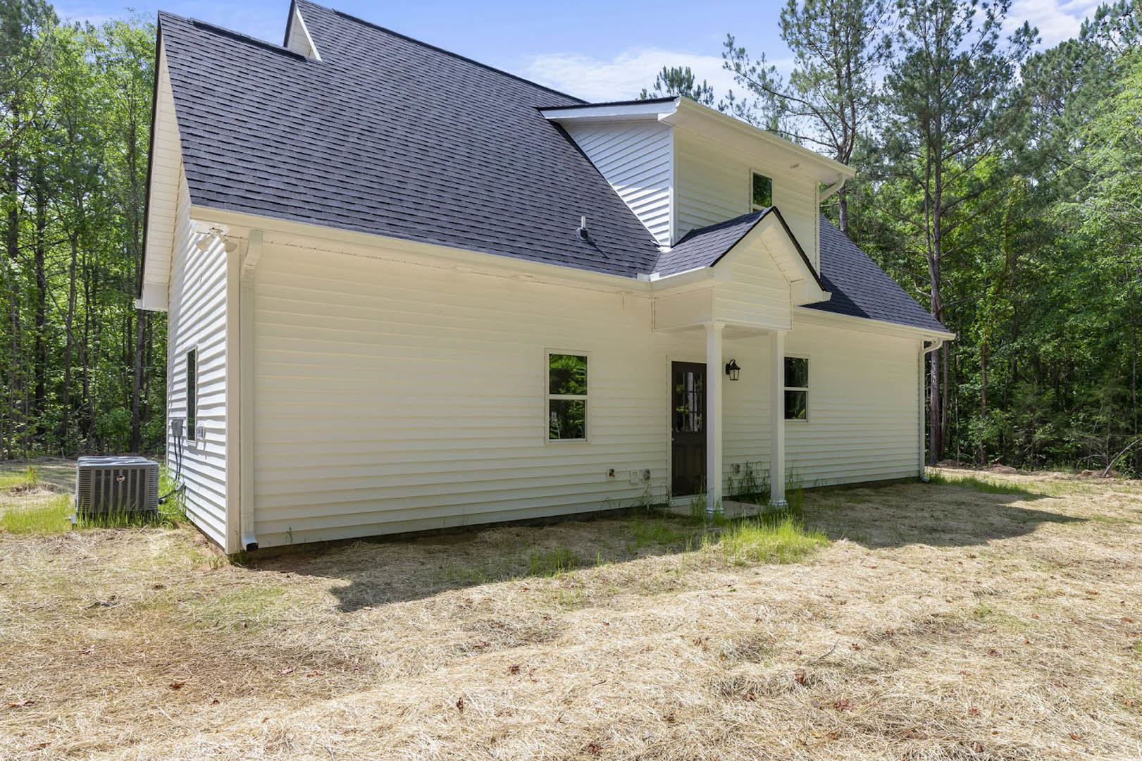 White house with black roof, barred front door, white-framed windows, grass yard with large metal box, mature trees in background