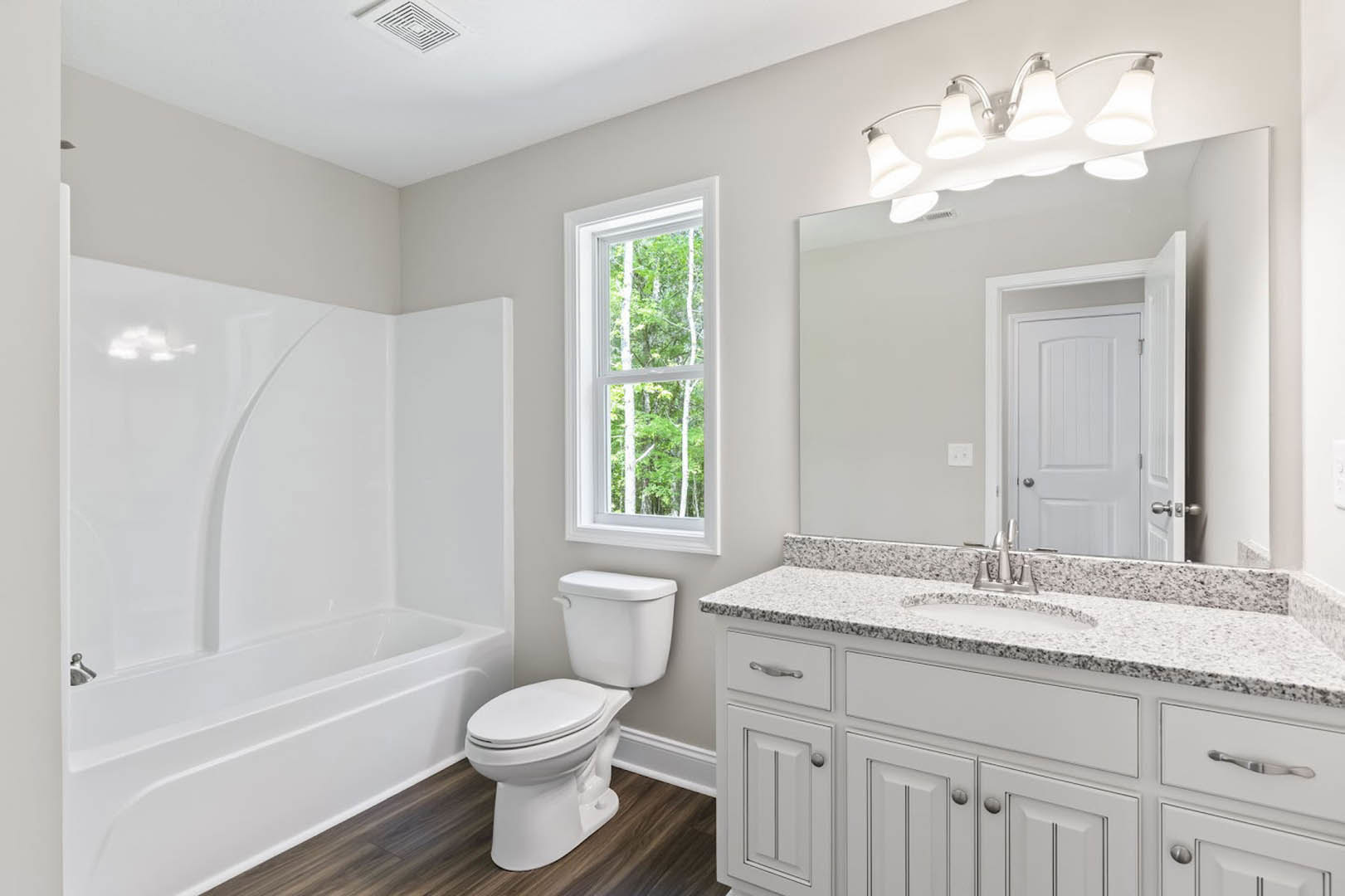 Modern bathroom with white porcelain sink, chrome faucet, wall-mounted mirror, white toilet, light gray tile walls, and window overlooking green trees