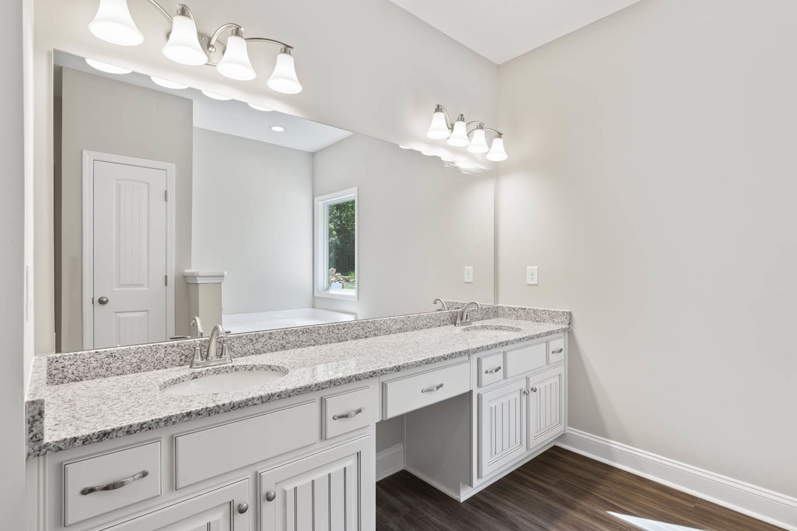Bathroom featuring a marble countertop, white cabinetry with silver handles, undermount sink, modern light fixture, and window overlooking trees.