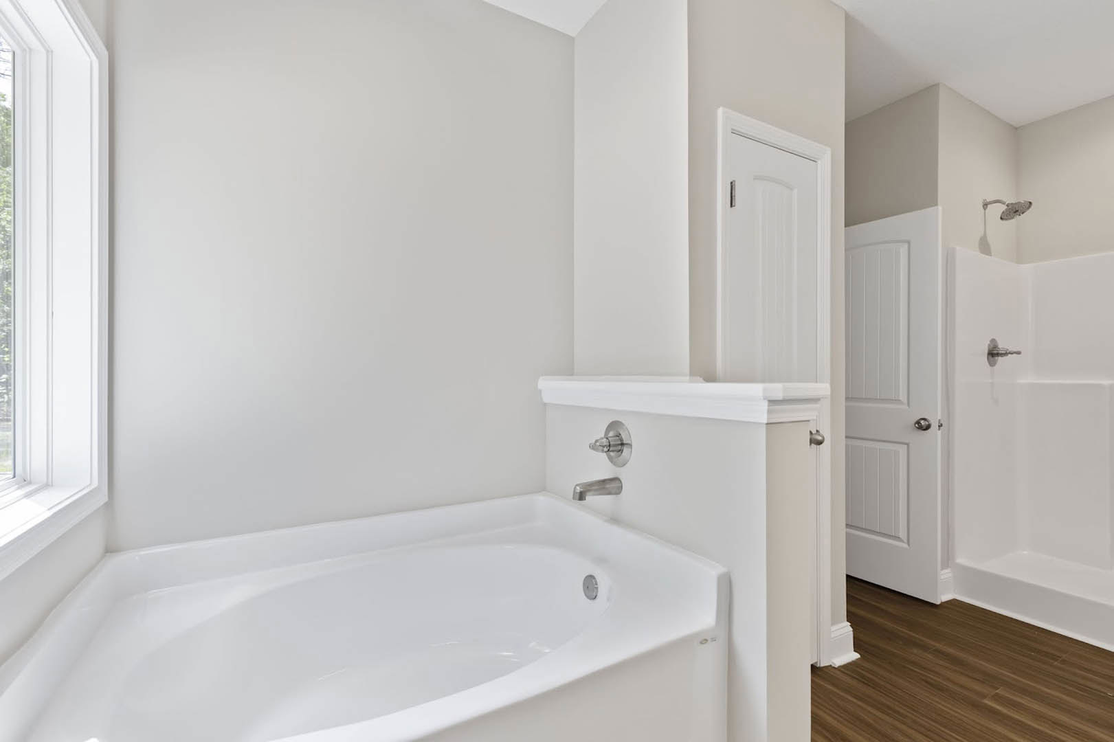 Freestanding white bathtub with chrome faucet on light tile floor, adjacent to white paneled door with brushed metal handle