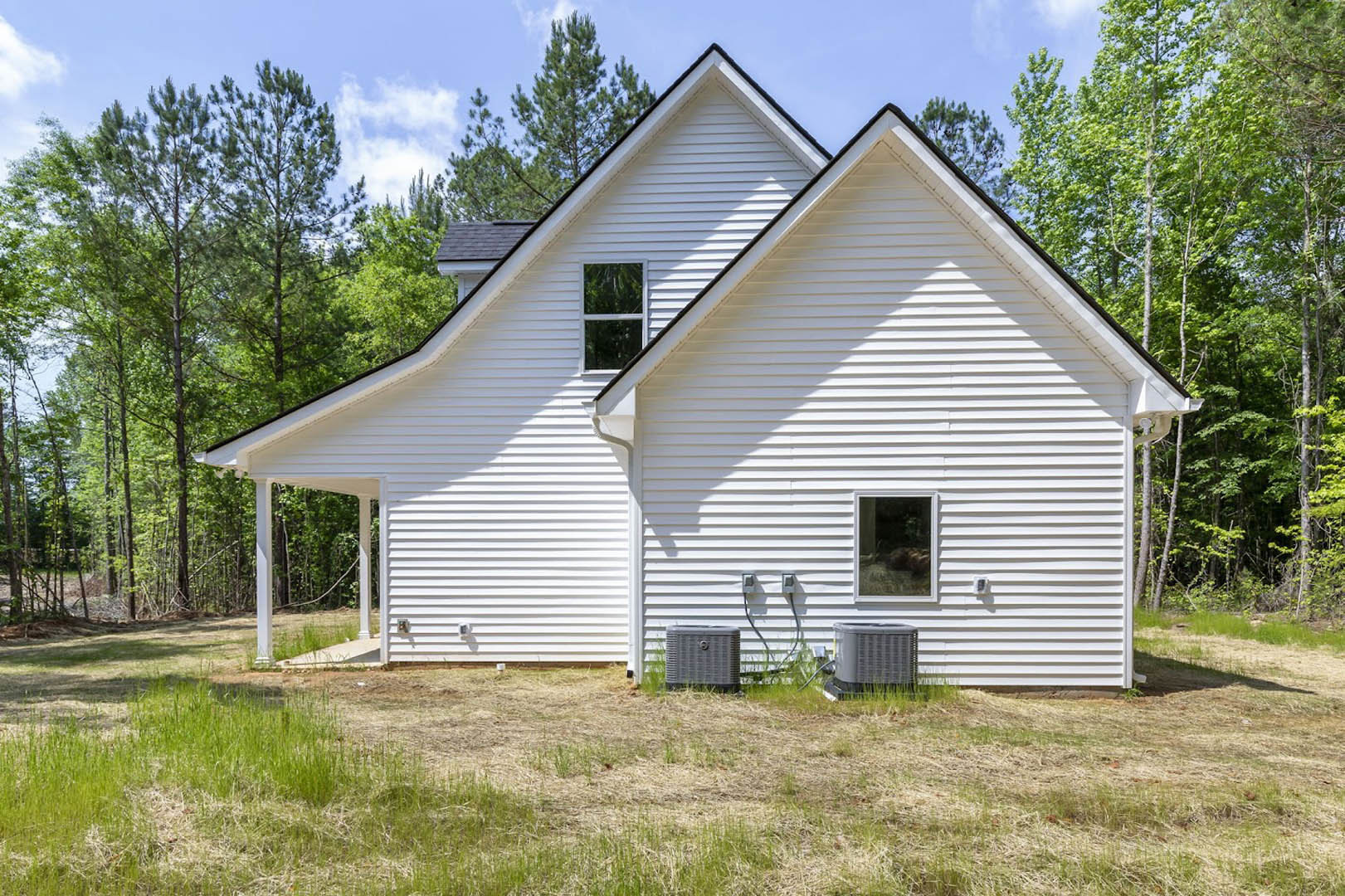 White metal roof atop a single-story house with light siding, front door, white-framed windows, grassy lawn, and surrounding trees.