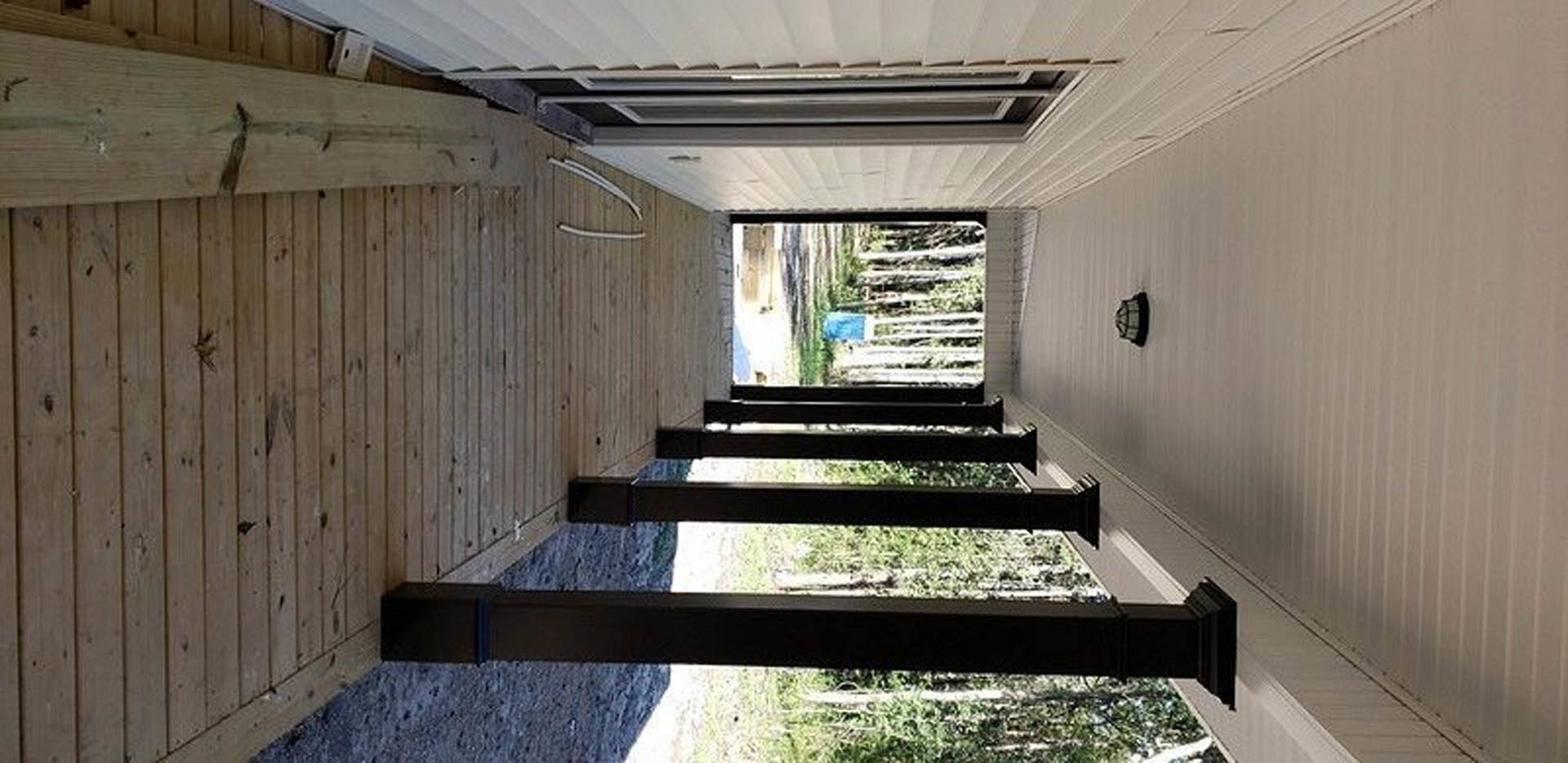 Front porch with white pillars, dark wood door, black bench, and green plants along composite material steps