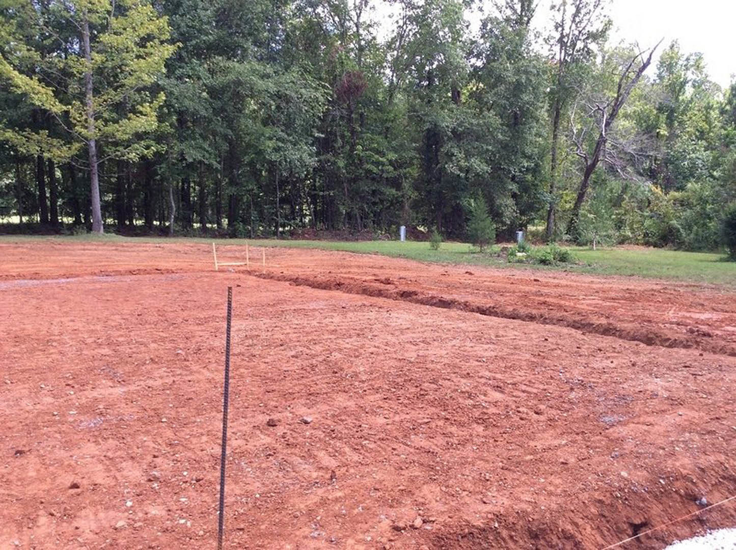 Dirt field bordered by trees and sparse grass, open sky above, undeveloped land lot