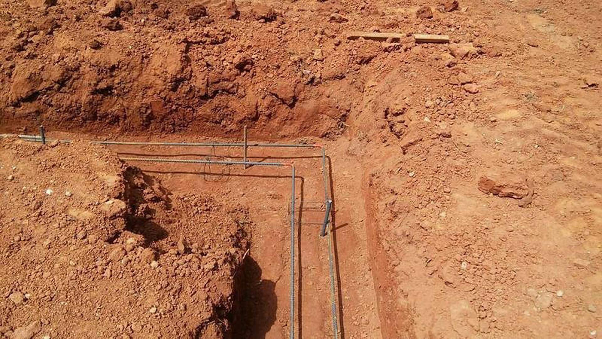 Exposed pipes laid across a dirt construction site with uneven soil and a partially dug hole