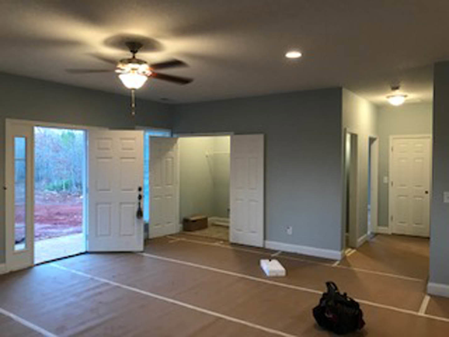 Room with wood laminate flooring, white door with black handle, ceiling fan, recessed ceiling light, and a black bag on the floor