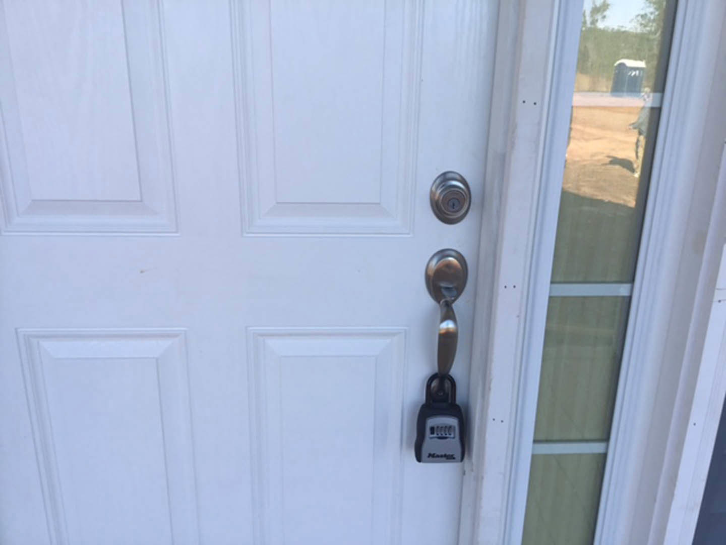 Dark wood exterior door with silver handle and lock, adjacent white-framed window, textured stucco wall.