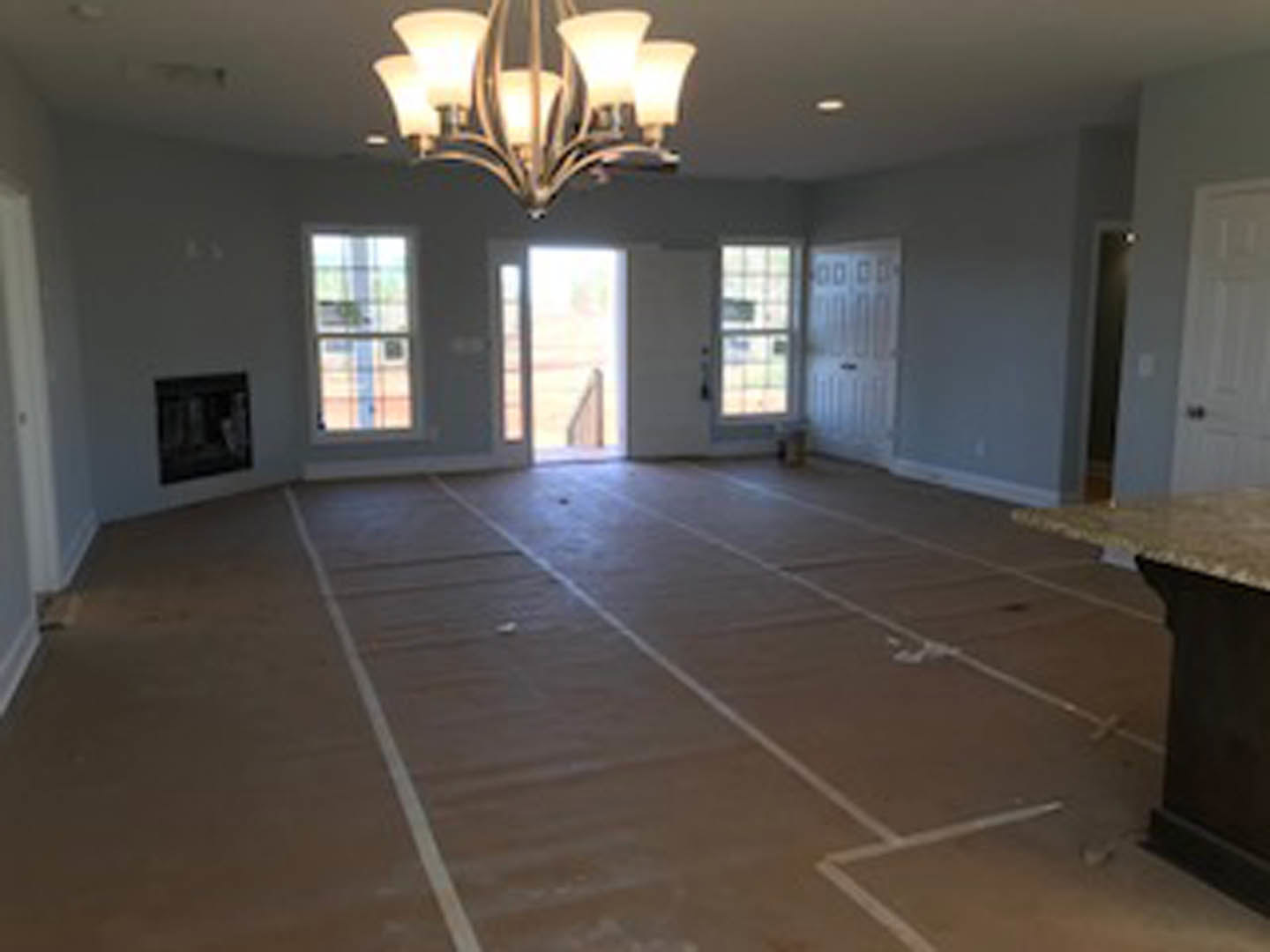 Living room with stone fireplace, ornate chandelier, wood flooring, and neutral walls