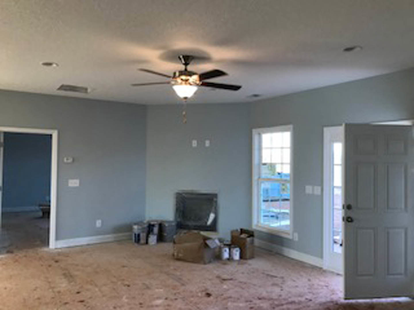 Living room with two ceiling fans, white plaster walls, light wood flooring, and a white door with a silver doorknob.