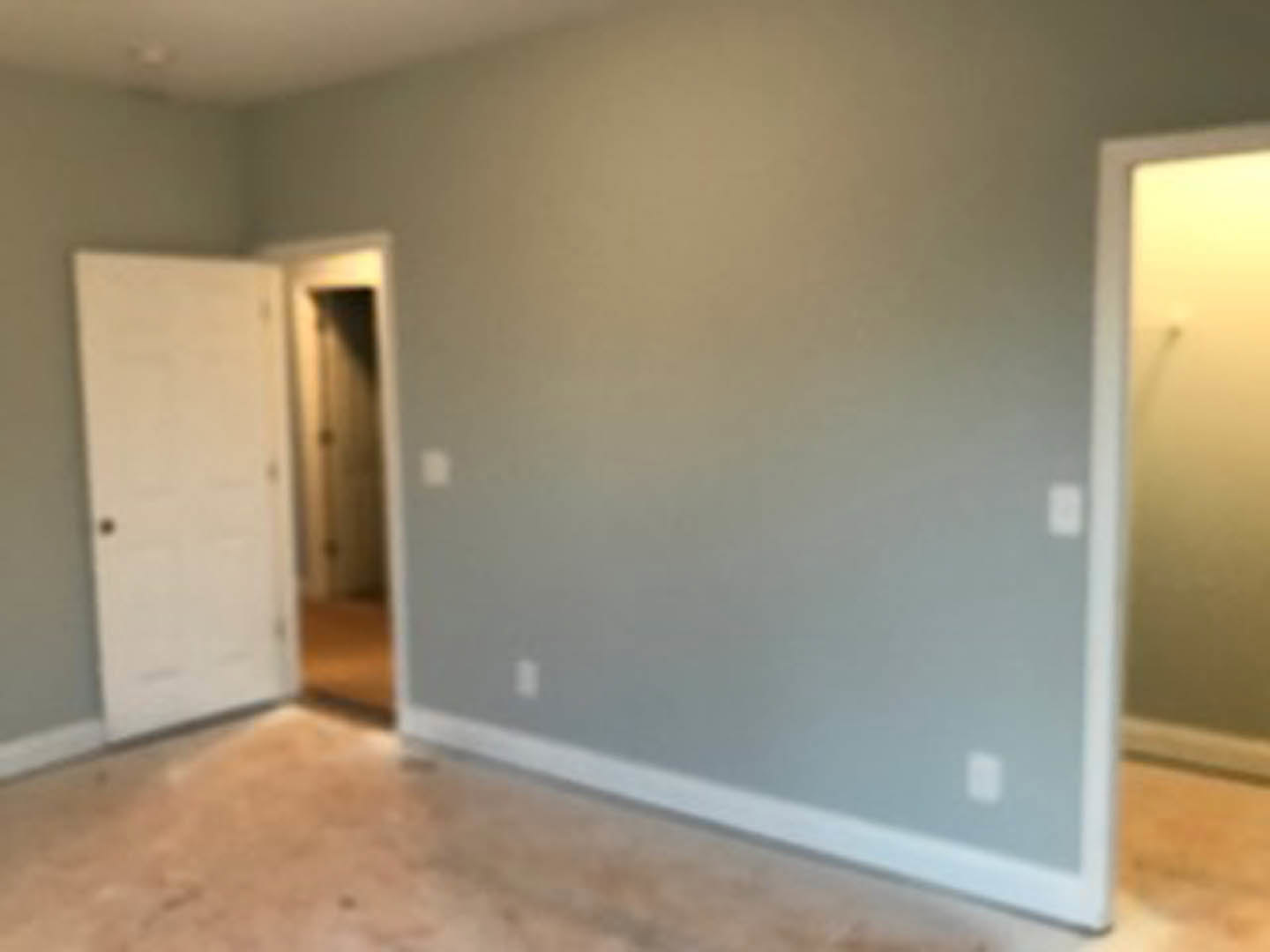 White-painted room with open door, gray flooring, smooth plaster walls, and recessed ceiling fixture