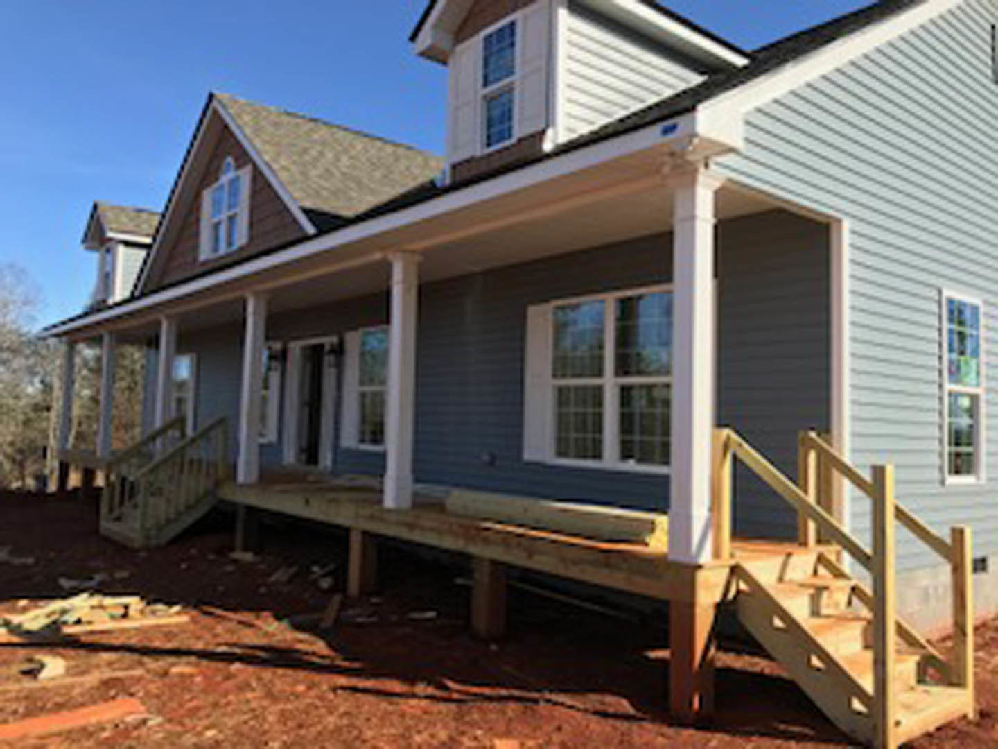Wooden porch with exposed beams, unfinished siding, and exterior staircase leading to a window on a custom home under construction