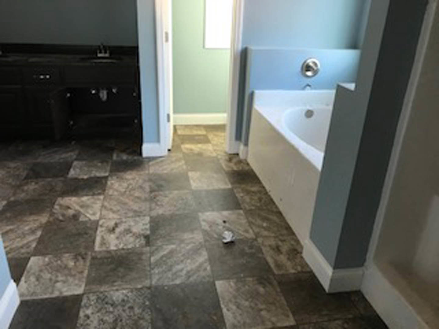 Modern bathroom with granite-topped vanity, undermount sink, freestanding white tub, tile flooring, and light wood cabinetry