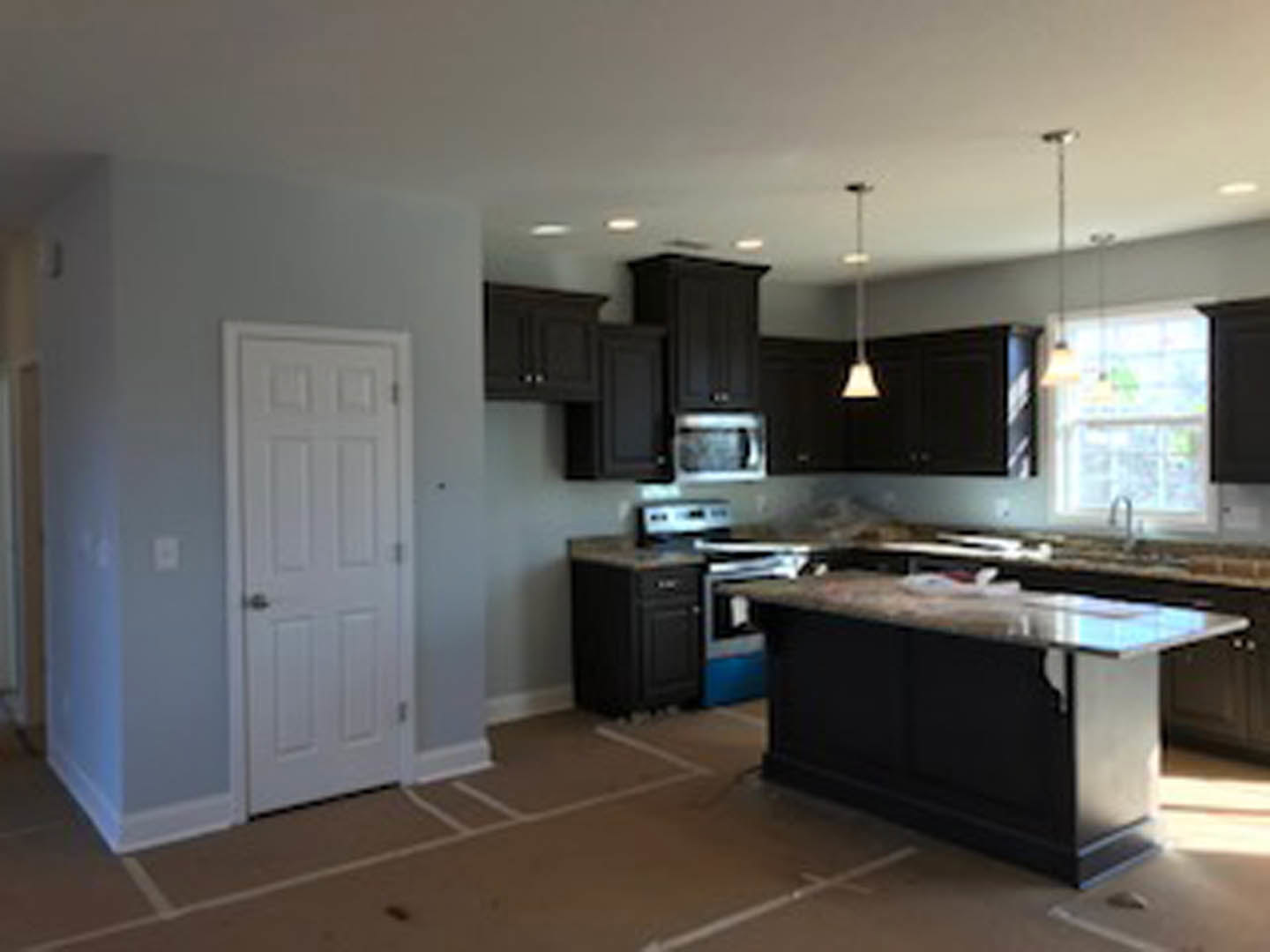 Kitchen with dark wood cabinets, marble-topped island, black countertops, stainless steel appliances, and light tile flooring