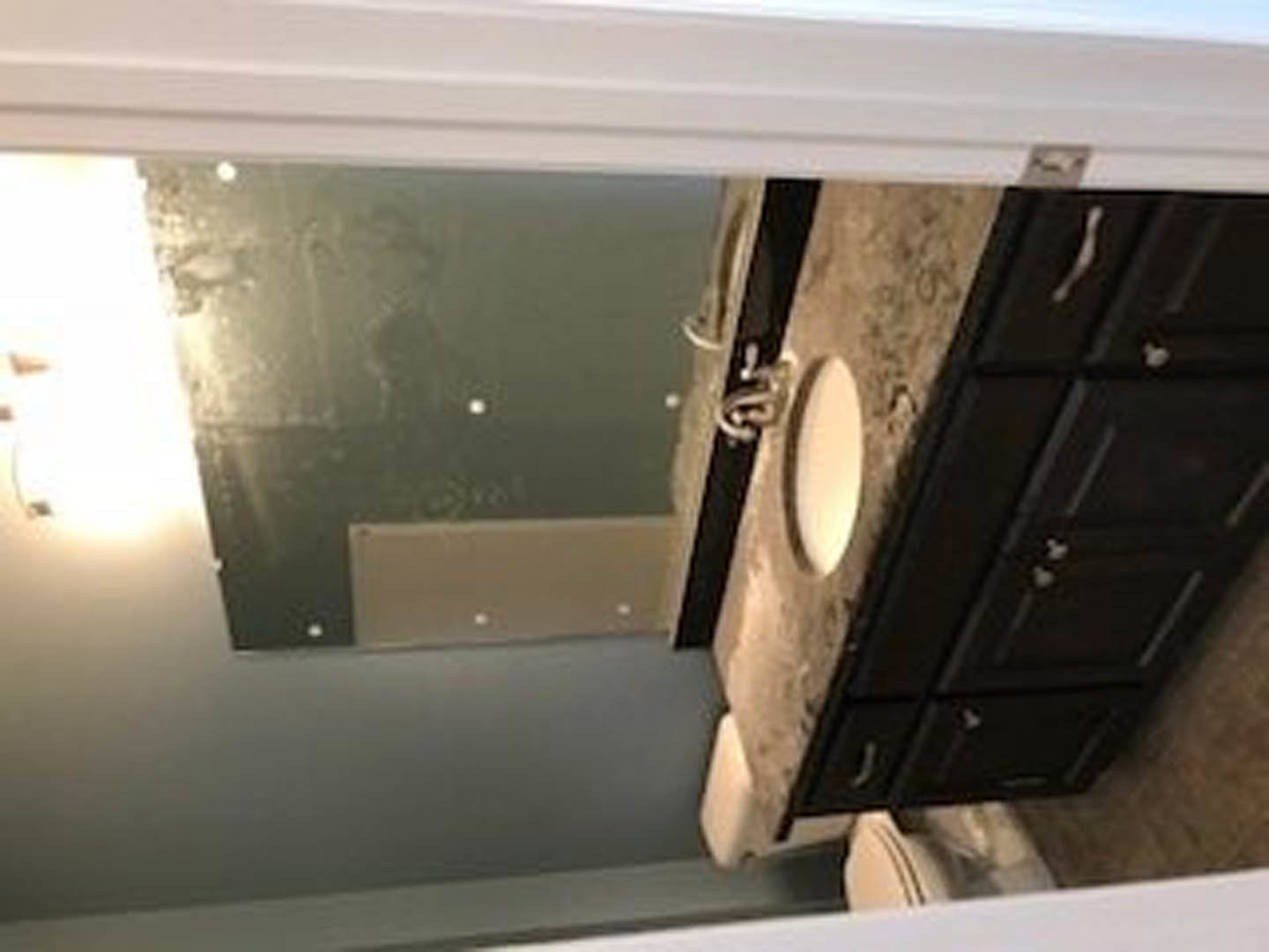 White bathroom with rectangular mirror above a wood vanity, integrated sink, and wall-mounted light fixture