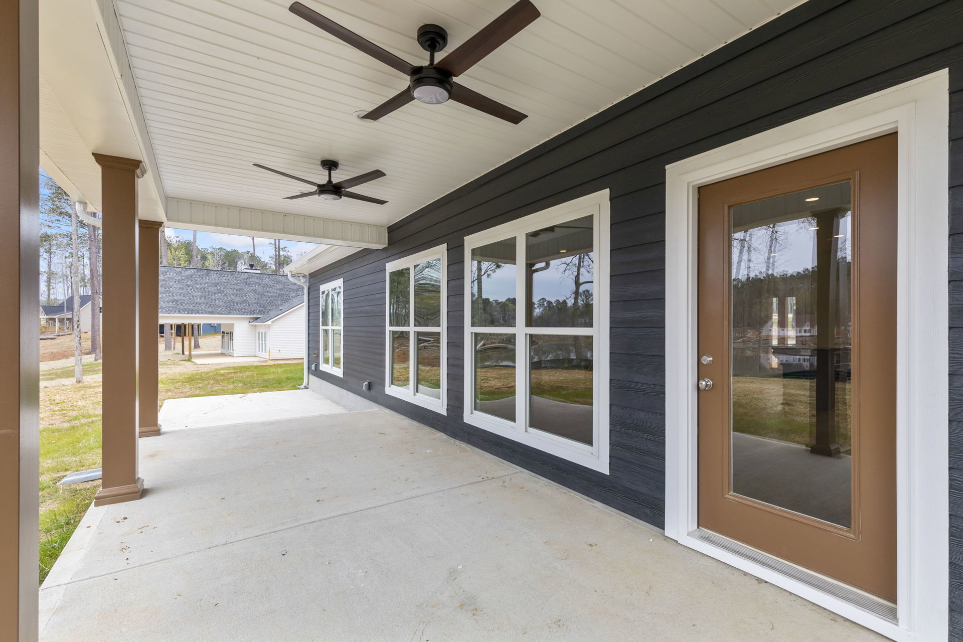 Front porch with white ceiling fan, brown door, white ceiling, and supporting posts; windows visible along exterior wall.