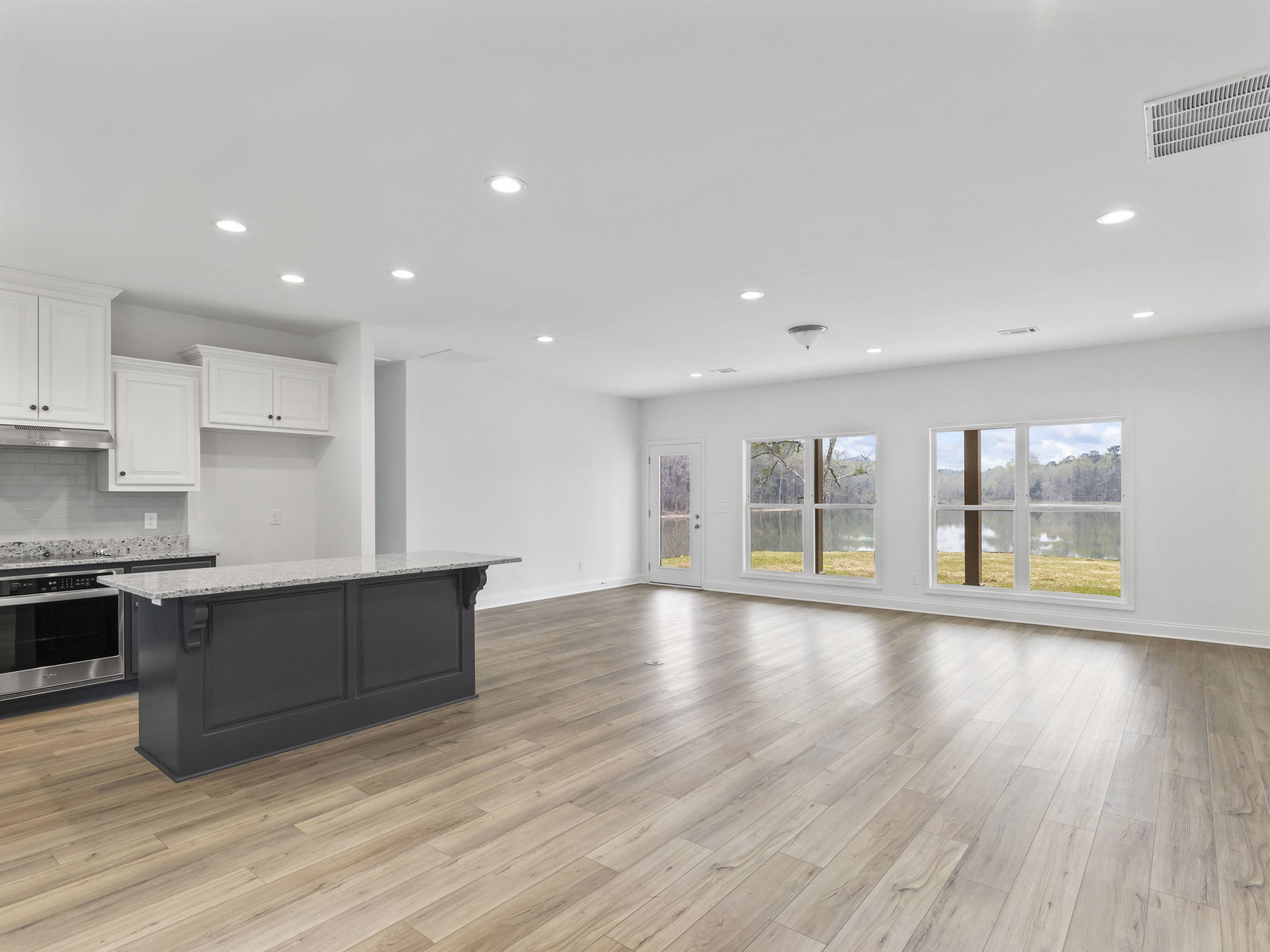 Open kitchen with white cabinetry, large central island, hardwood flooring, ceiling vent, and window overlooking lake and trees