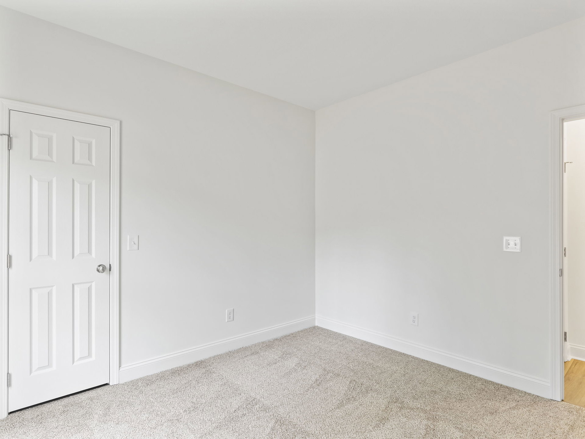 White carpeted room with white walls, white door featuring silver knob, and white door frame