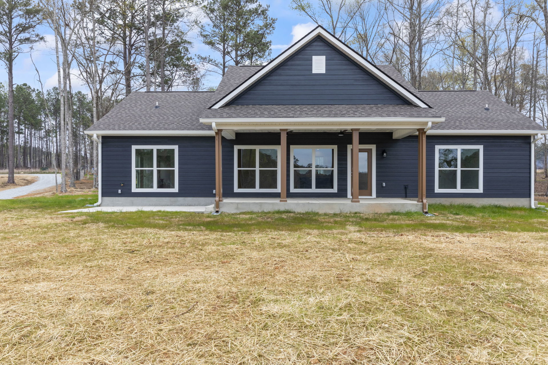 Blue siding house with white trim, large windows, concrete porch, manicured lawn, mature trees in background, clear sky above
