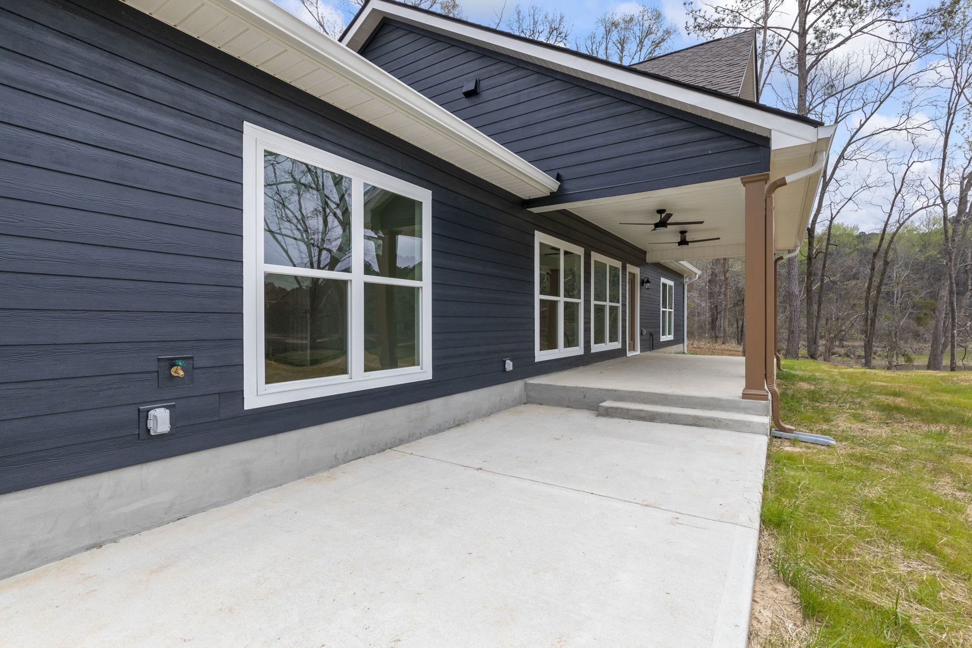 Two-story house with light siding, covered porch, concrete patio, white-framed windows, grassy yard, and concrete steps leading to the entrance.
