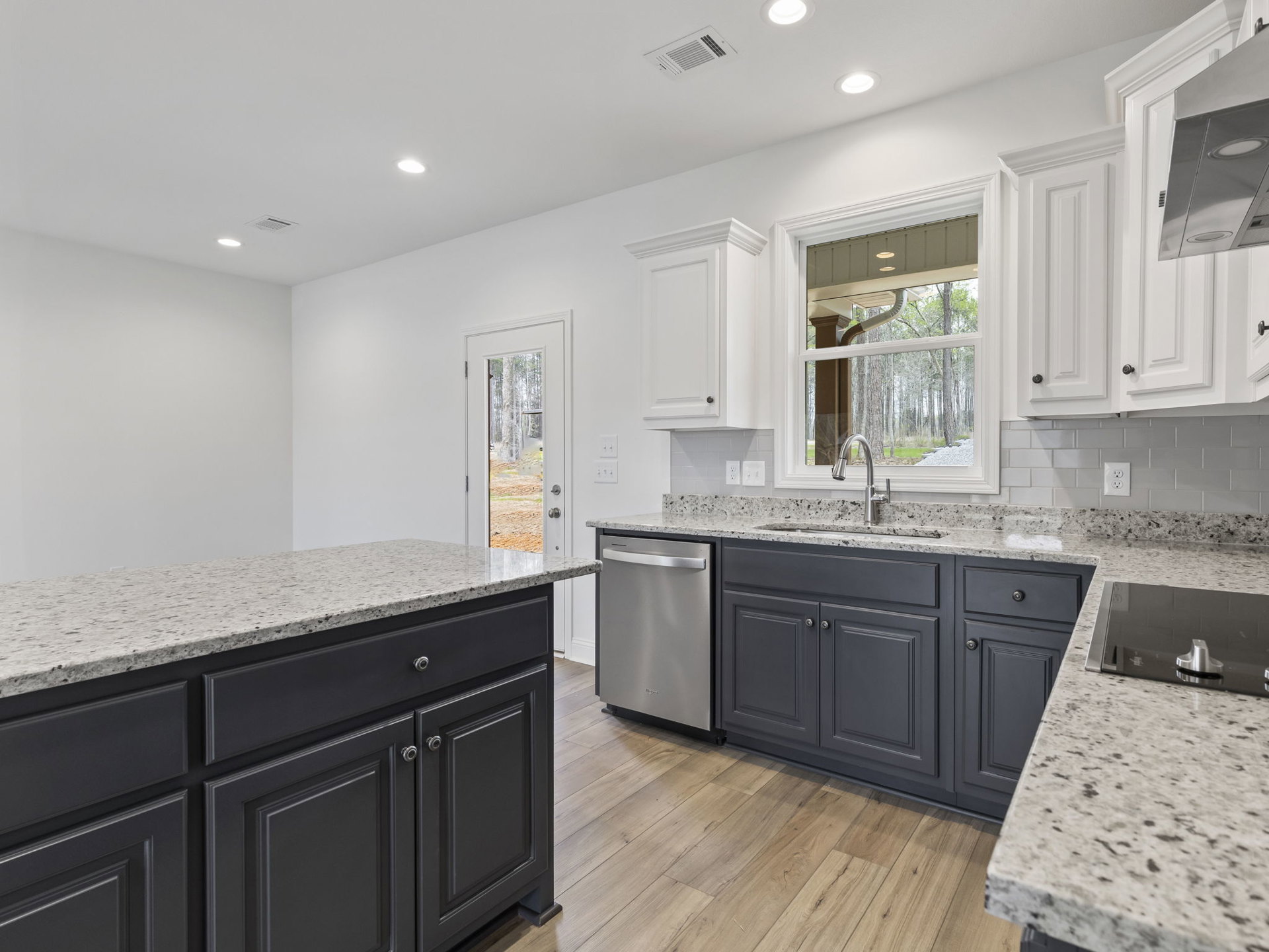 Granite countertops with tile backsplash, stainless steel dishwasher, white cabinetry, undermount sink, and vent hood in a modern kitchen