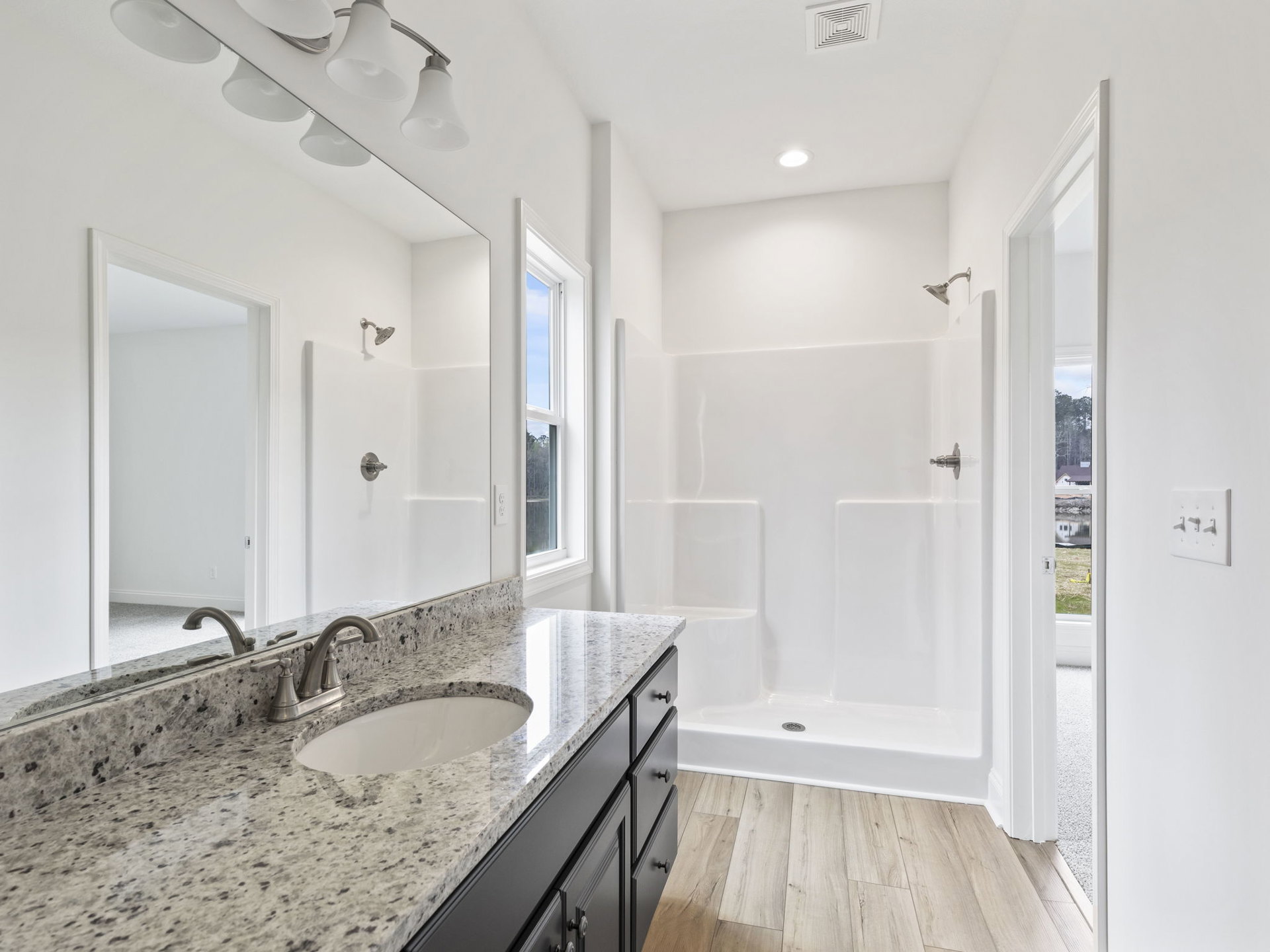Marble countertop with white undermount sink and black speckled surface, chrome faucet, tiled shower with wall-mounted shower head, ceiling vent, and neutral tile finishes