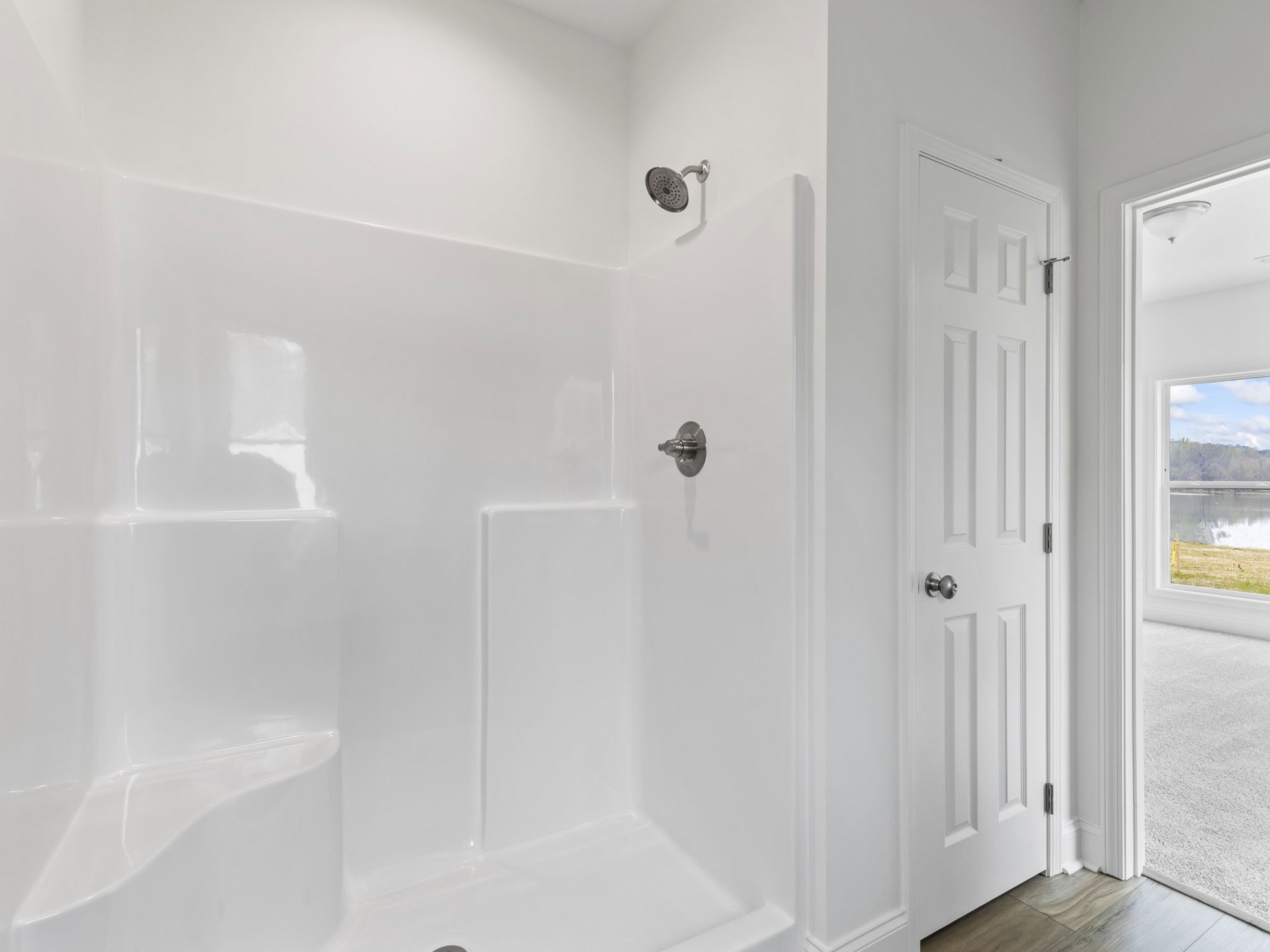 White tile shower with chrome showerhead, wood flooring, and white door frame in modern bathroom.