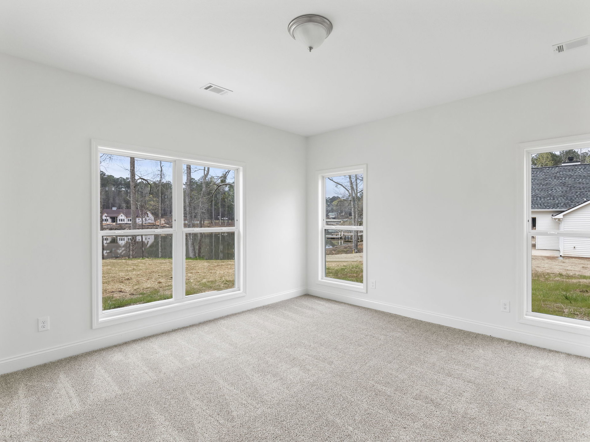 Bright room with white carpet, white walls, large window overlooking house and trees, ceiling light fixture