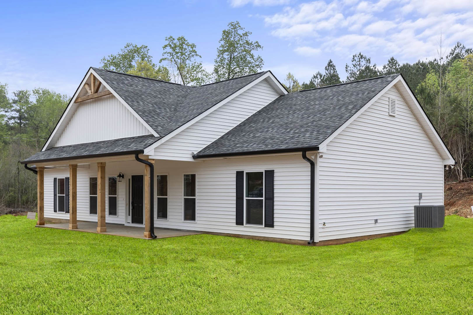 White siding house with black roof, white-framed windows, manicured green lawn, blue sky with scattered clouds, mature trees in background