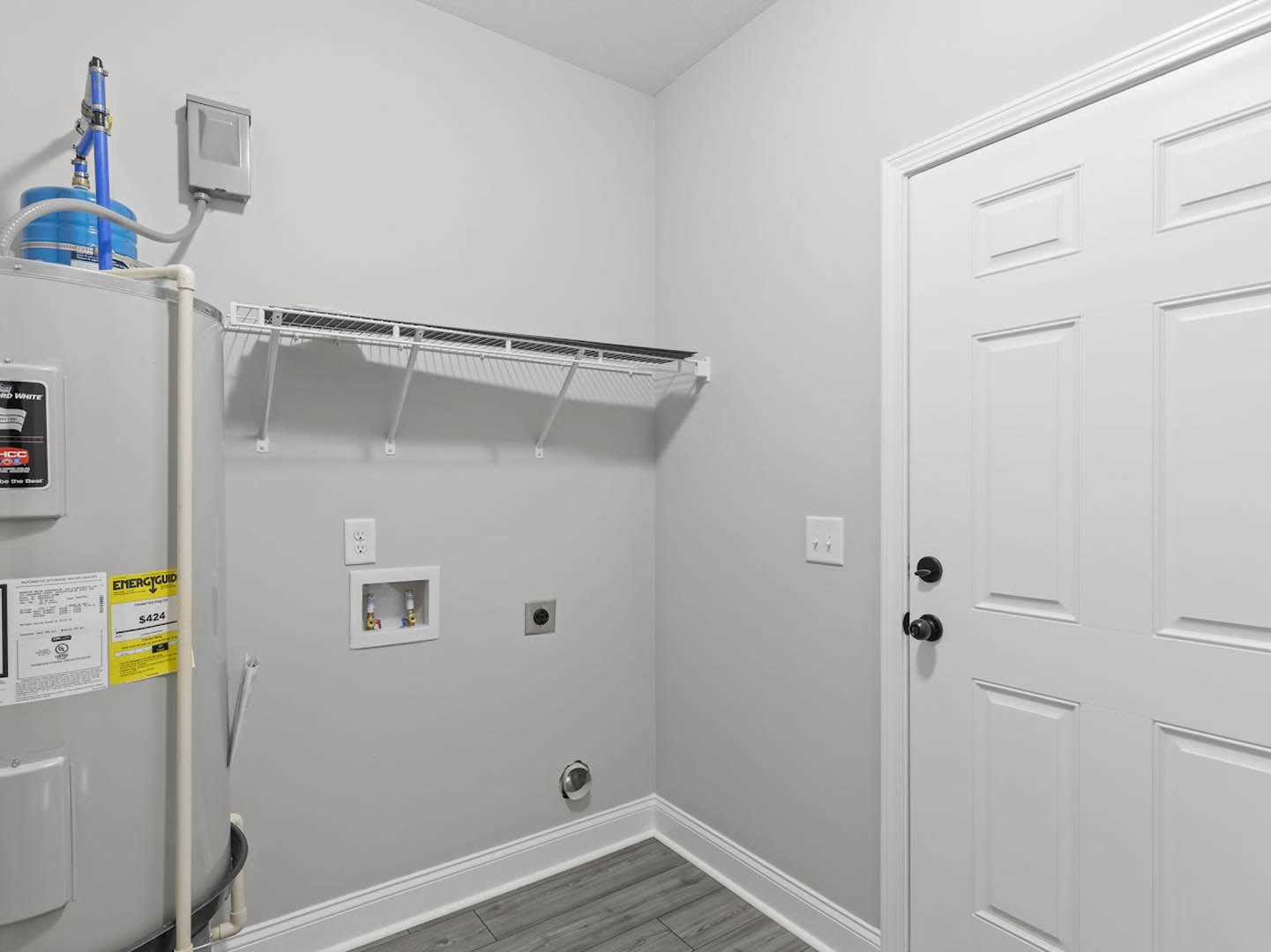 White paneled door with black knobs, built-in white shelving, light switch on white wall, yellow and white sign, white utility box with exposed pipes, refrigerator partially