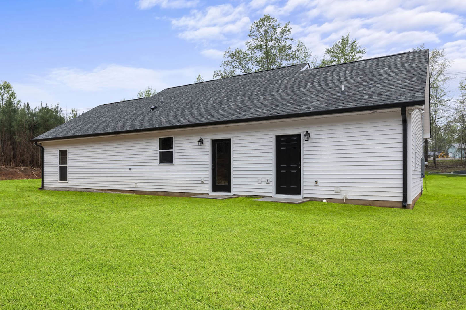 White farmhouse-style exterior with black front door, white trim, glass panel door, large windows, manicured green lawn, and cloudy sky.
