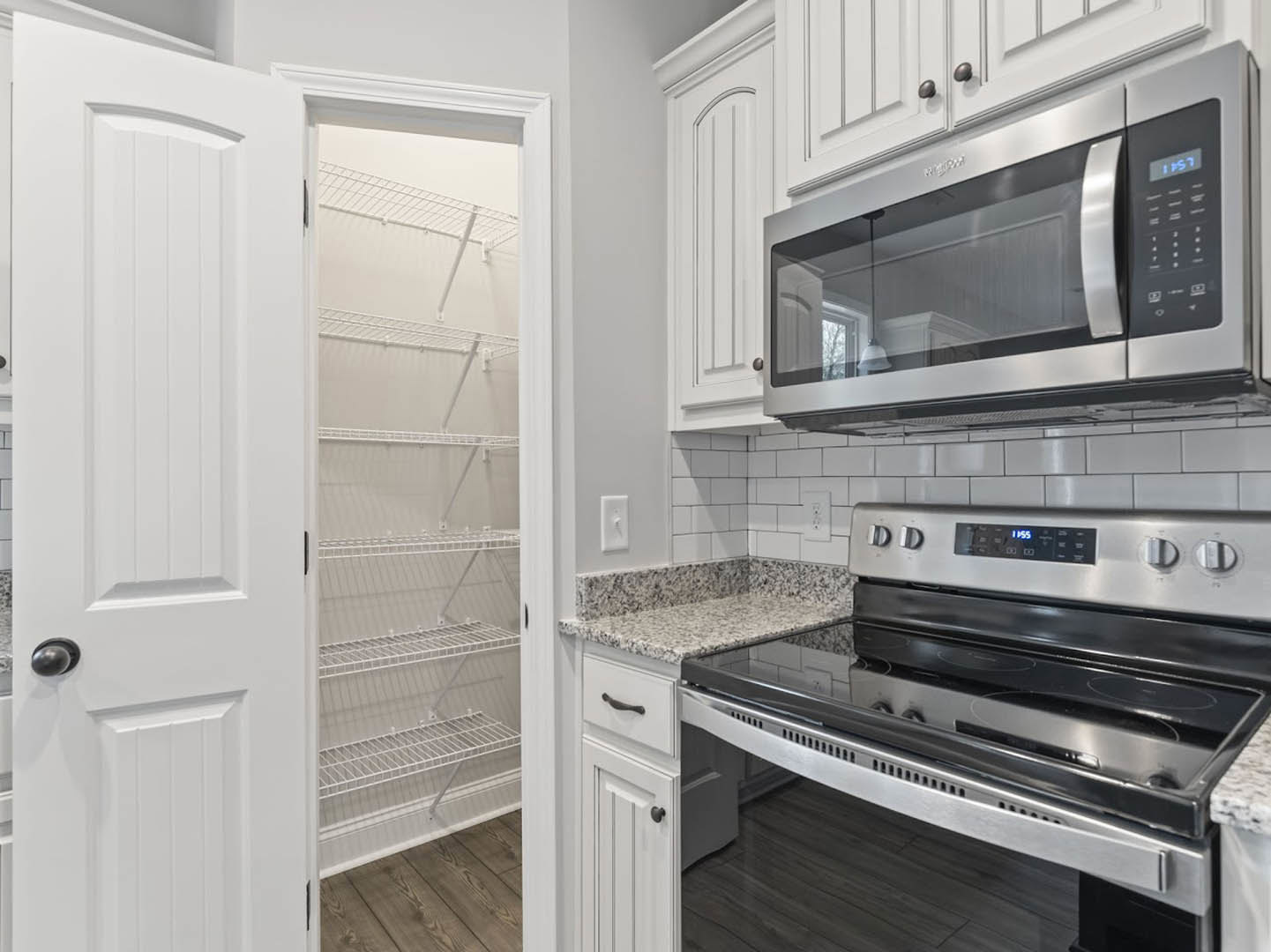 Modern kitchen with white cabinetry, built-in microwave oven above a stove with digital display, open refrigerator door, open shelving, and light-colored countertops