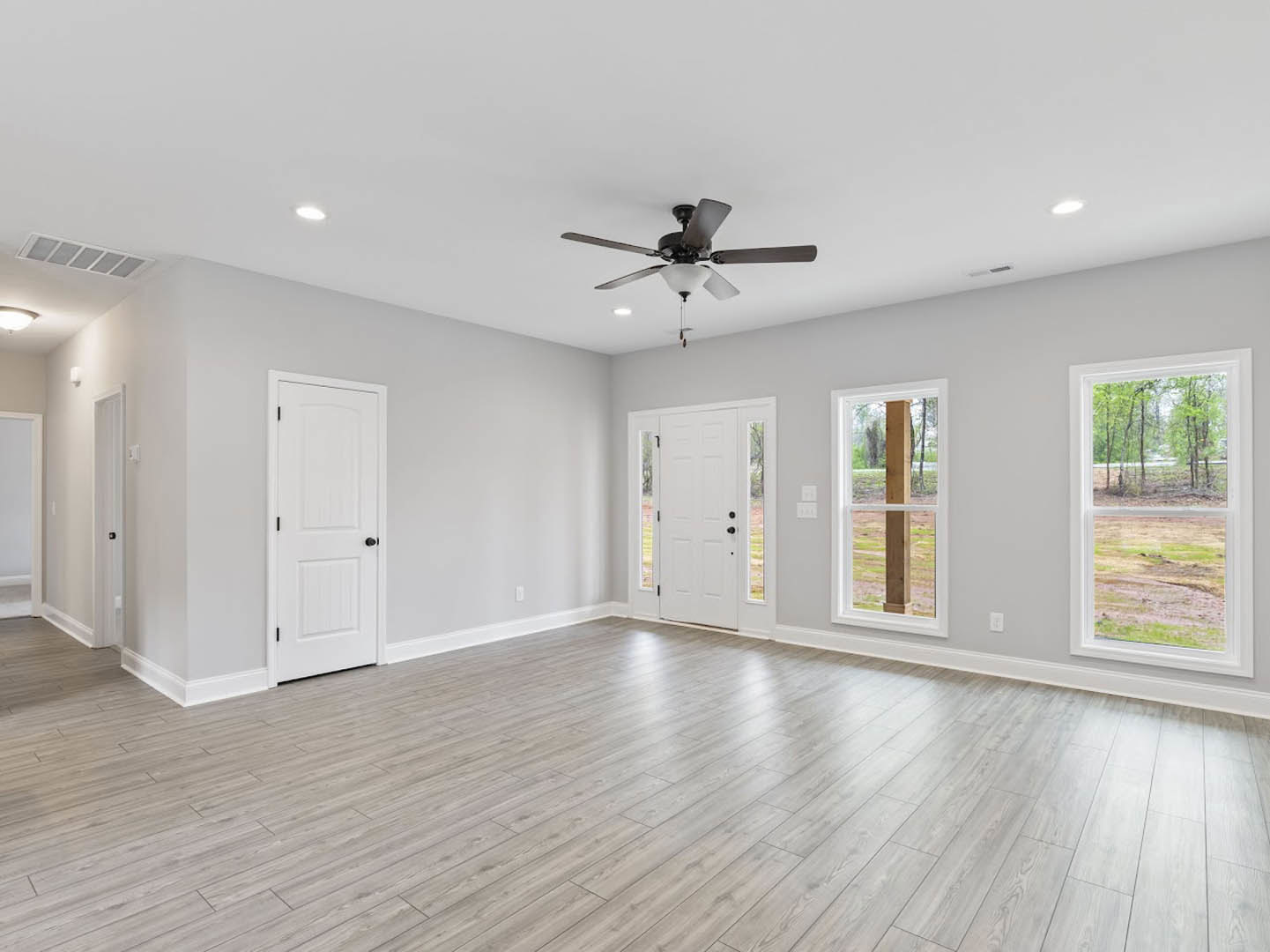 Hardwood floor room featuring white doors with black knobs, a ceiling fan with light, white door with glass panels, and window overlooking outdoors