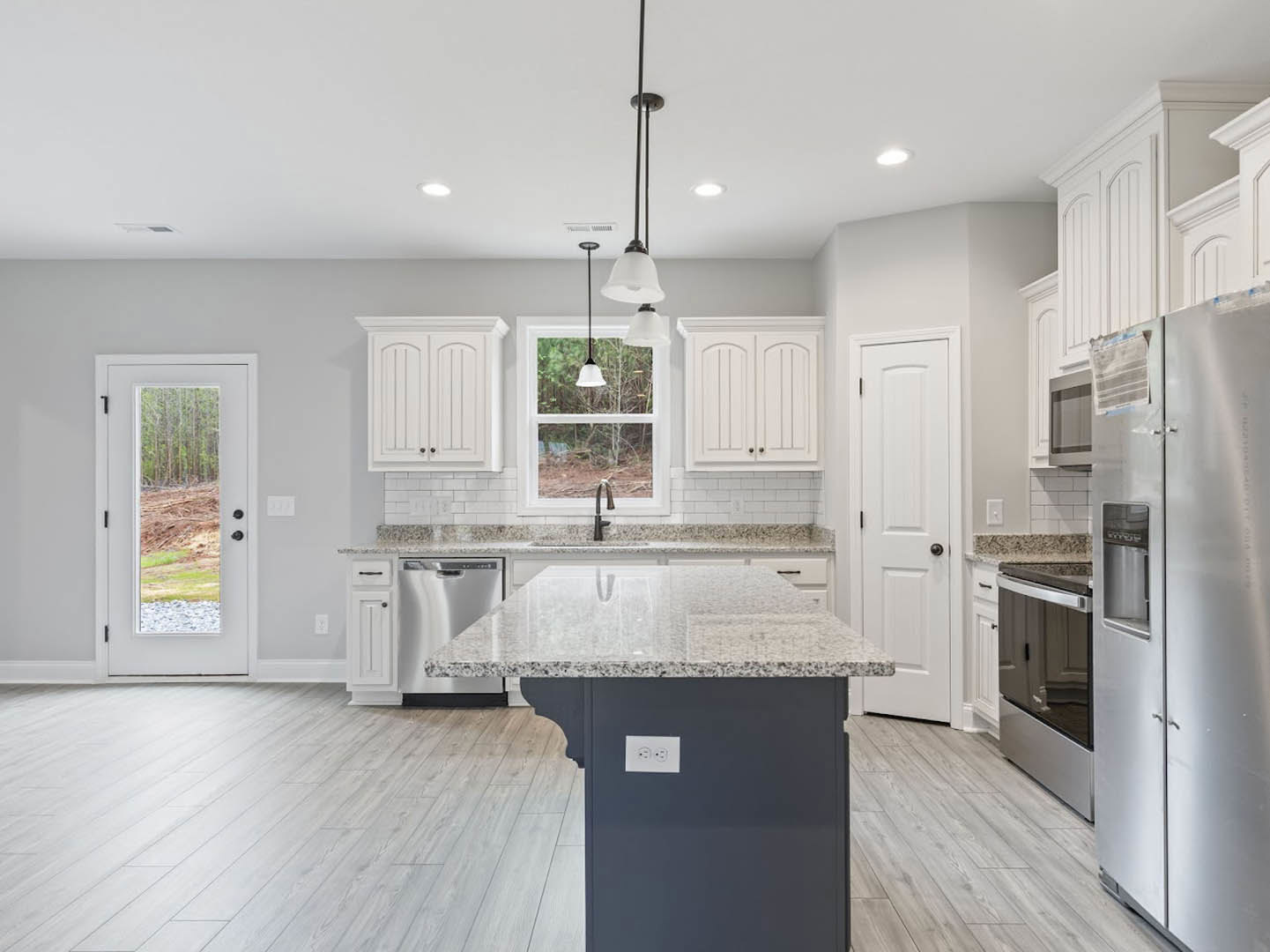 Open kitchen with white cabinetry, central island featuring quartz countertop, stainless steel refrigerator and range, undermount sink, light wood flooring, and a door with forest
