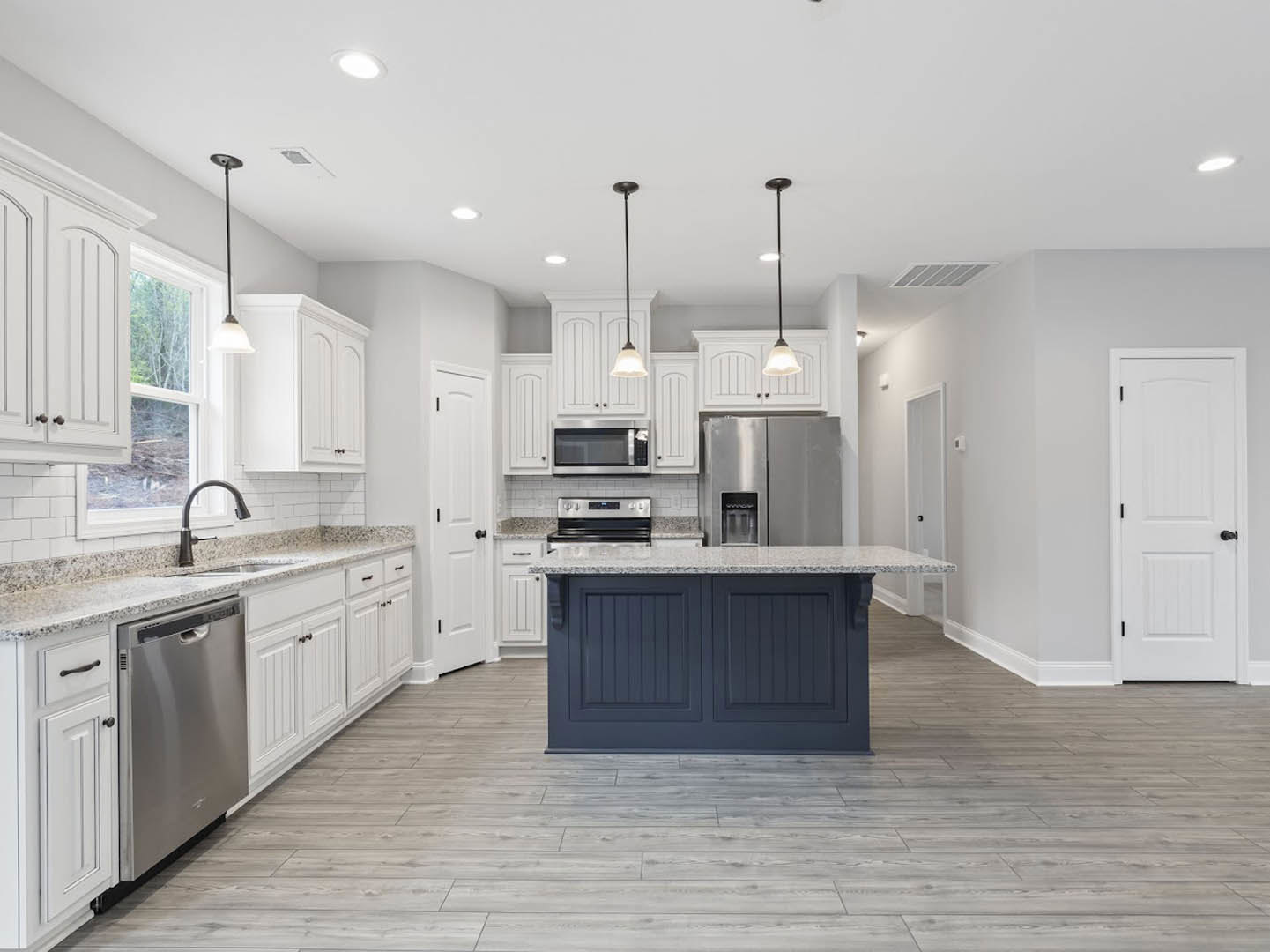 Spacious kitchen featuring a large central island with quartz countertop, stainless steel refrigerator and microwave, white cabinetry with black hardware, tile backsplash, and